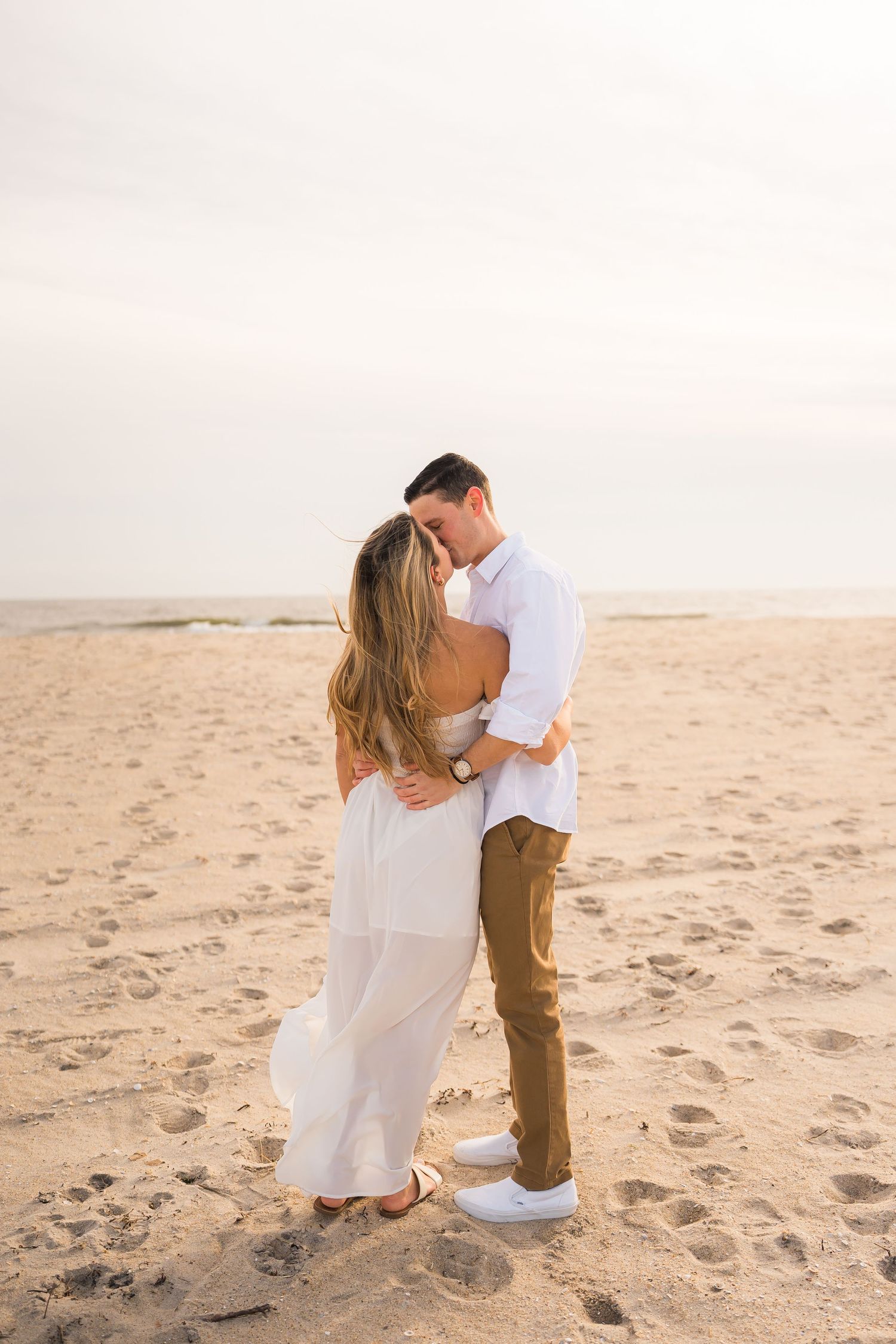 Couple embracing on a sandy beach during golden hour.