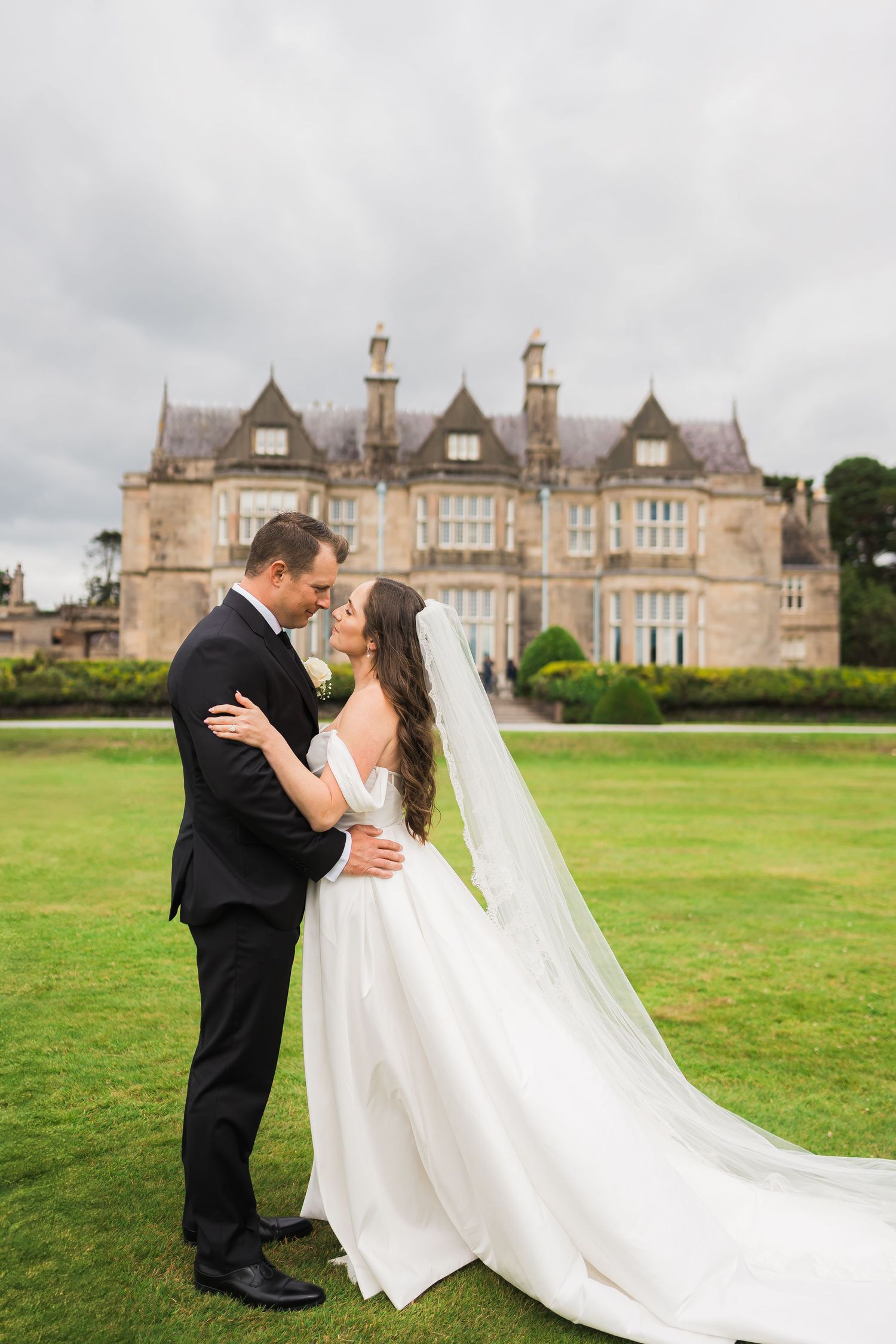 A romantic wedding portrait on the lawn of a grand Victorian-style mansion with stunning architecture.