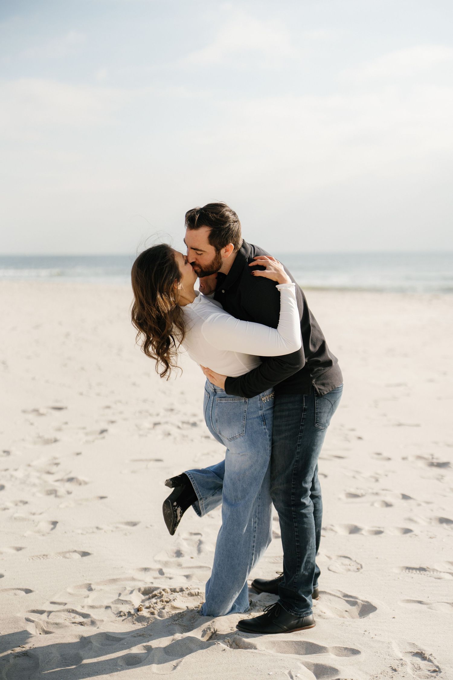 Romantic couple sharing an intimate moment while embracing on a serene beach with soft sand and ocean backdrop.
