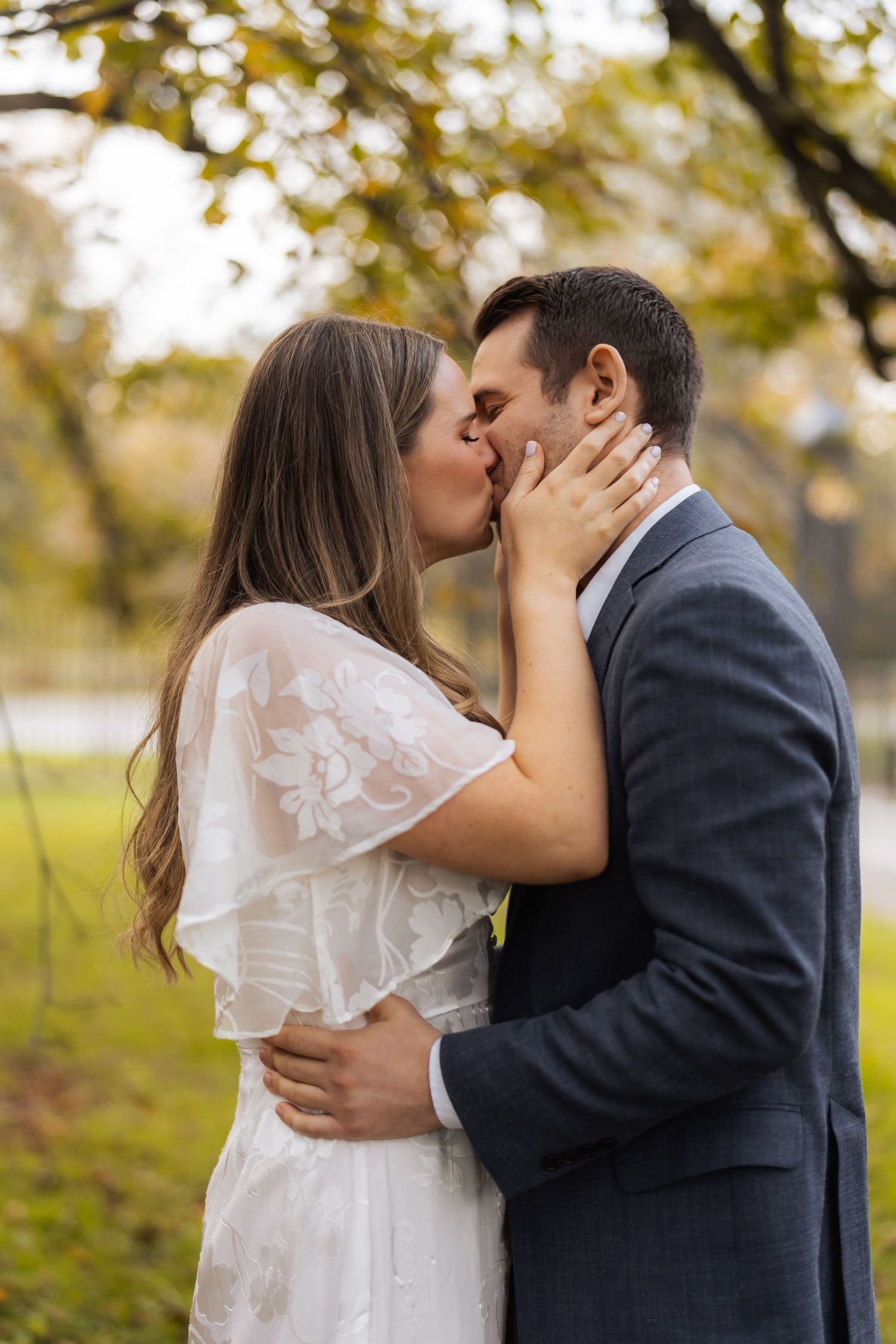 A romantic wedding couple shares a tender kiss outdoors during autumn with golden leaves in the background.