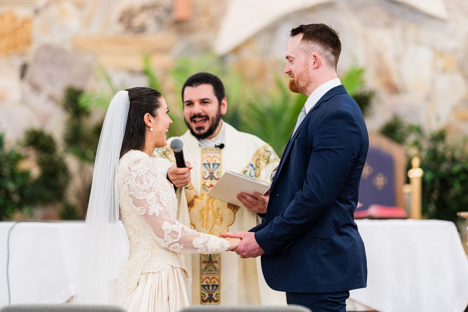 A couple exchanges vows during an outdoor wedding ceremony with a white altar backdrop.