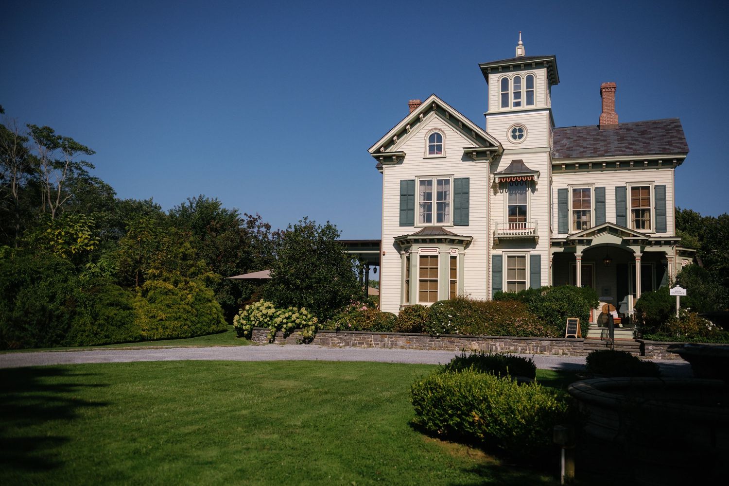 Historic white Victorian farmhouse with wrap-around porch stands proudly against a clear blue sky.