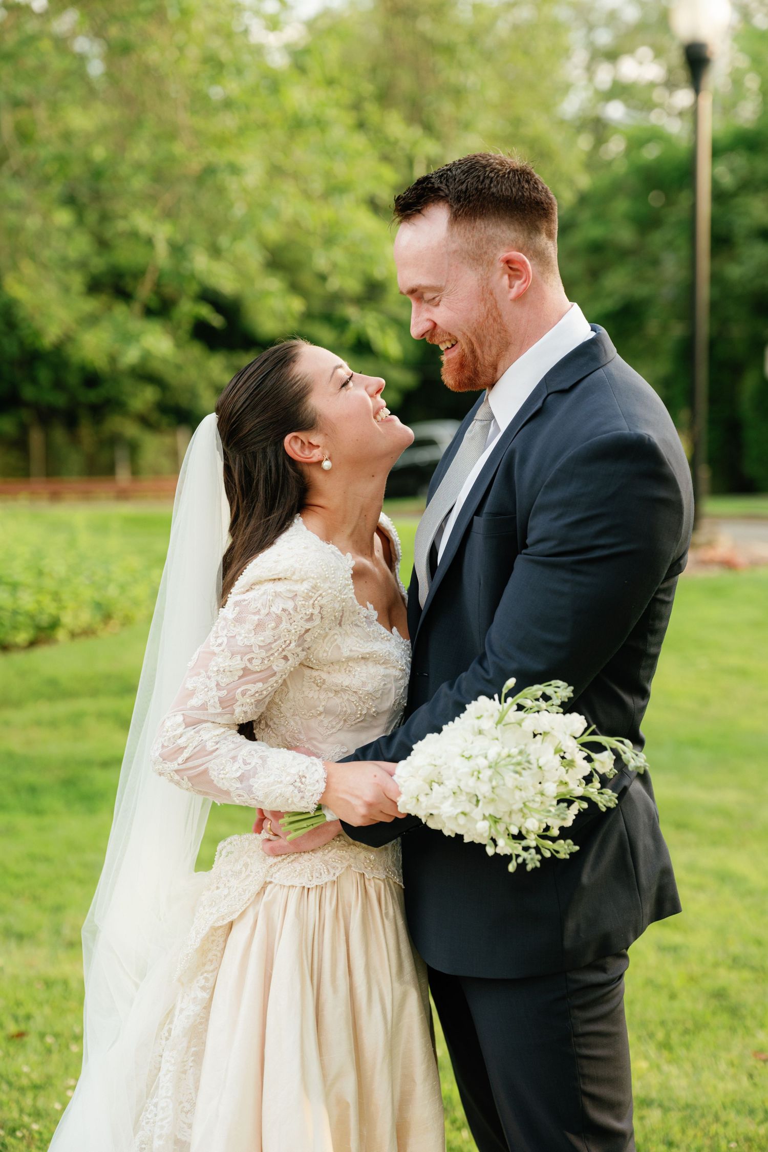 A romantic wedding photoshoot shows a couple embracing outdoors in a garden setting with lush greenery.