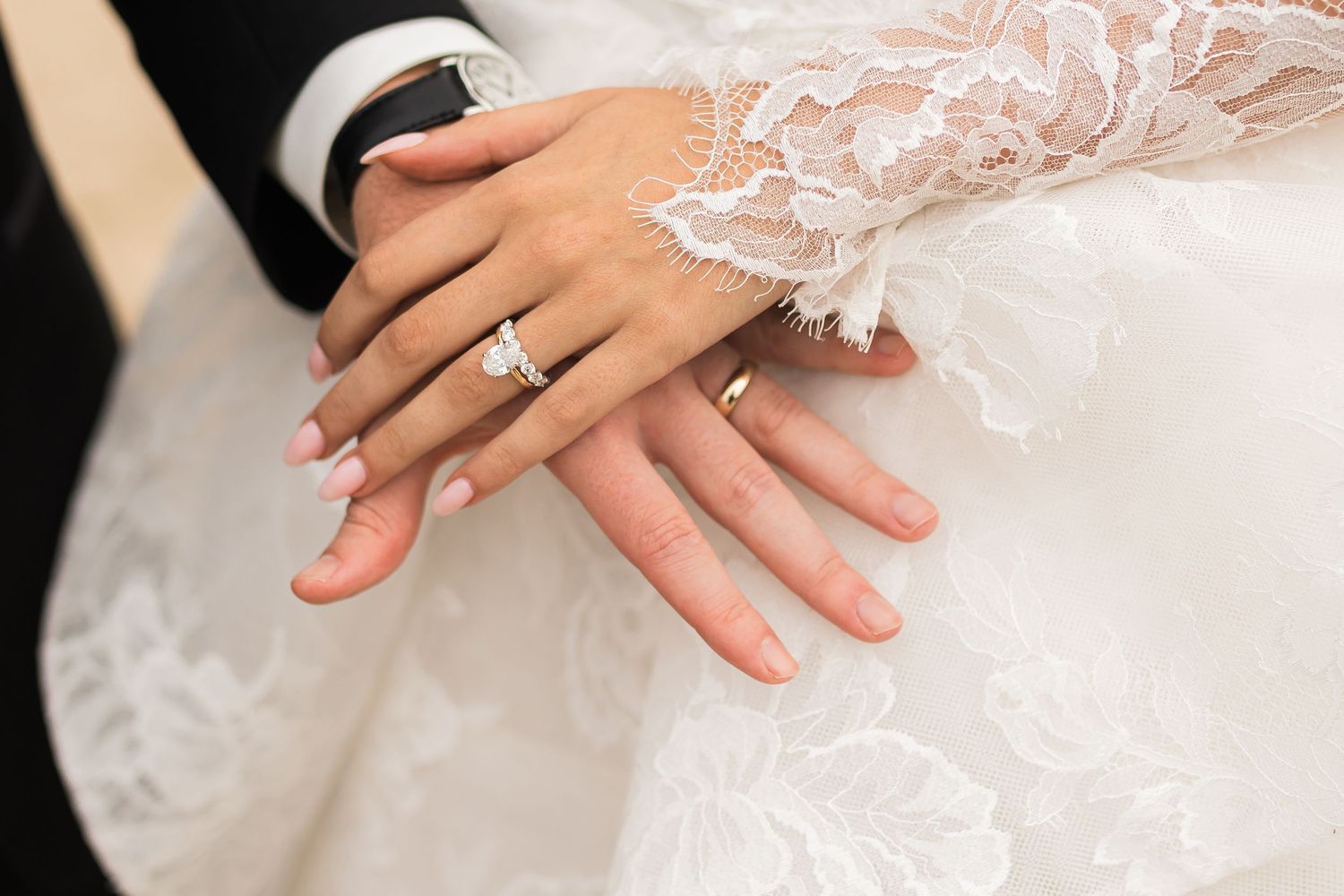 Close up of newlywed hands showing wedding rings against white lace dress fabric.