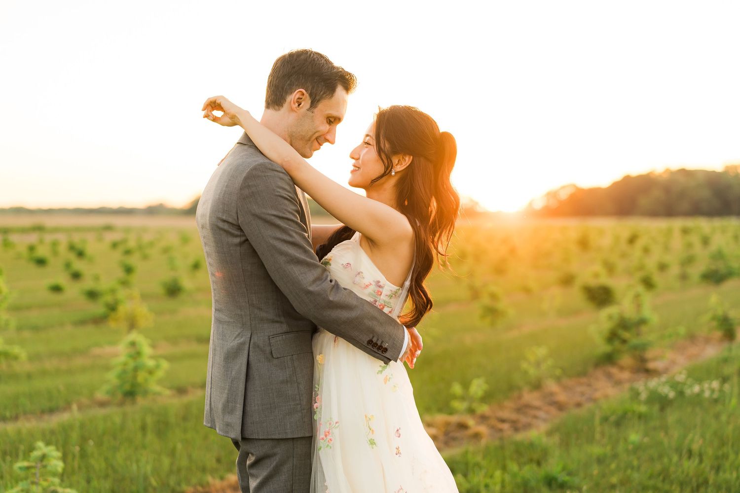 A couple embraces in a golden sunset field during their wedding.