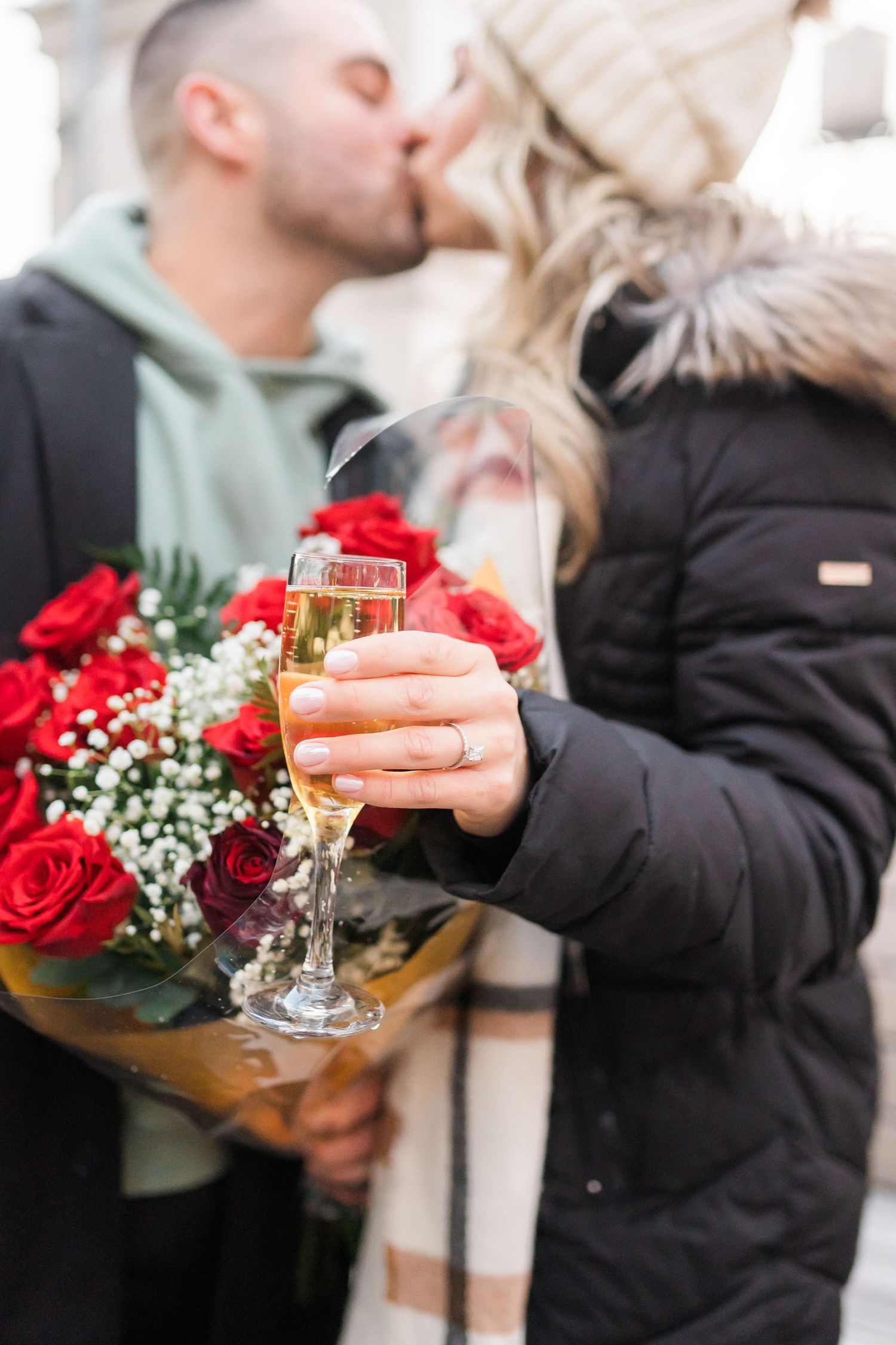 A close-up of champagne and red roses being held during a romantic winter moment.