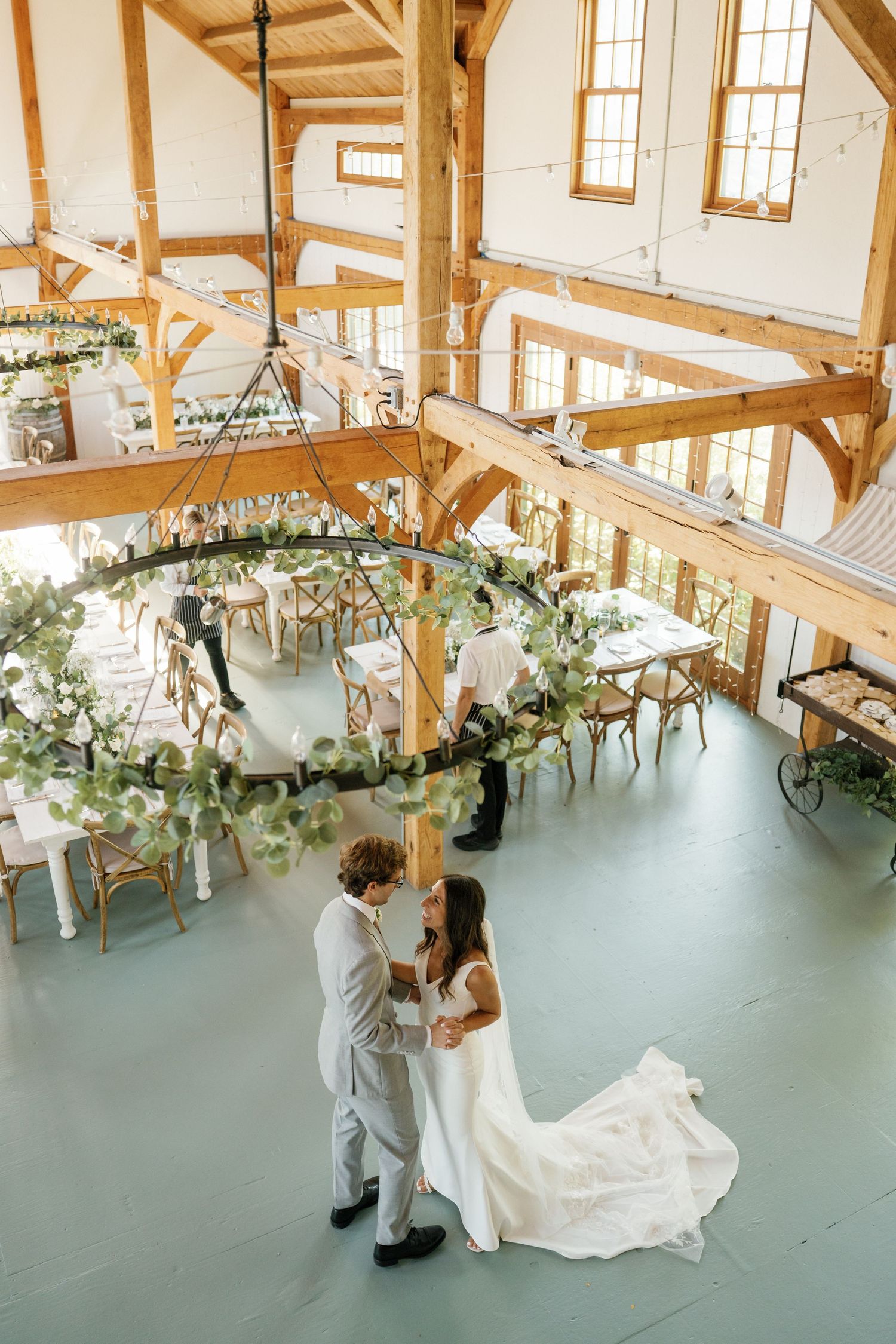A couple shares an intimate dance moment in a rustic barn venue decorated with elegant greenery and natural light.