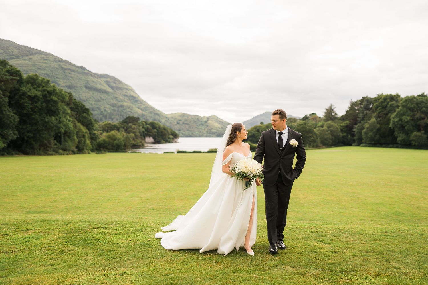 A wedding photo on a lush green lawn with mountains and a lake in the background in Ireland.