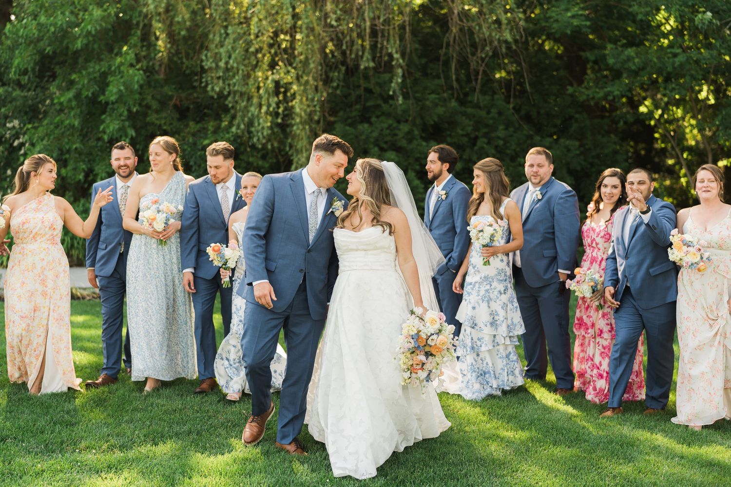 Wedding party poses together on a sunny garden lawn with trees in background.