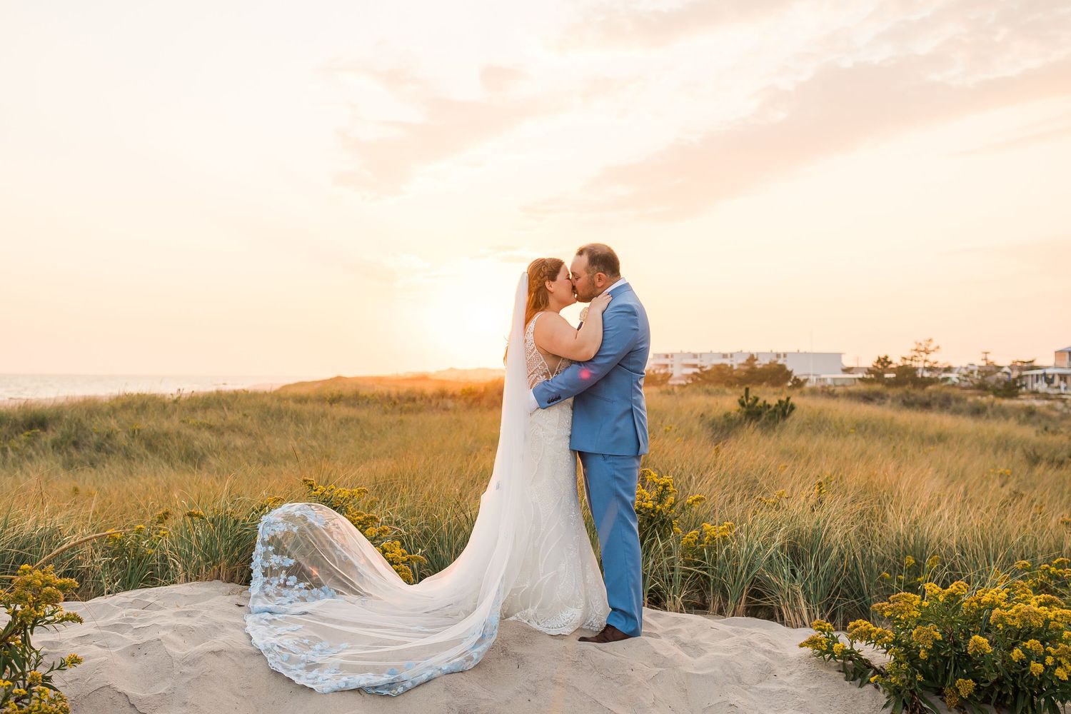 A romantic sunset wedding portrait with flowing dress train and coastal landscape in background.