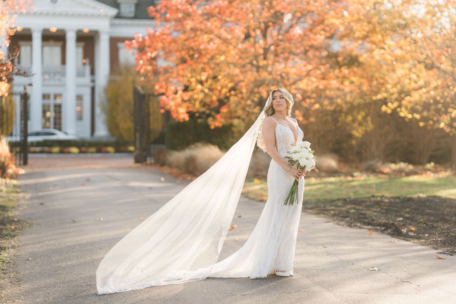 A wedding moment captured during autumn with beautiful orange foliage and a classical white building in the background.
