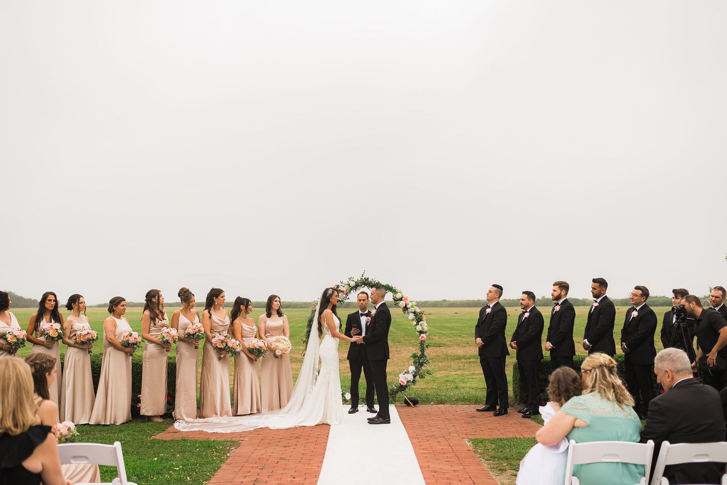 Wedding ceremony on white aisle runner with bridesmaids in gold dresses and groomsmen in dark suits.