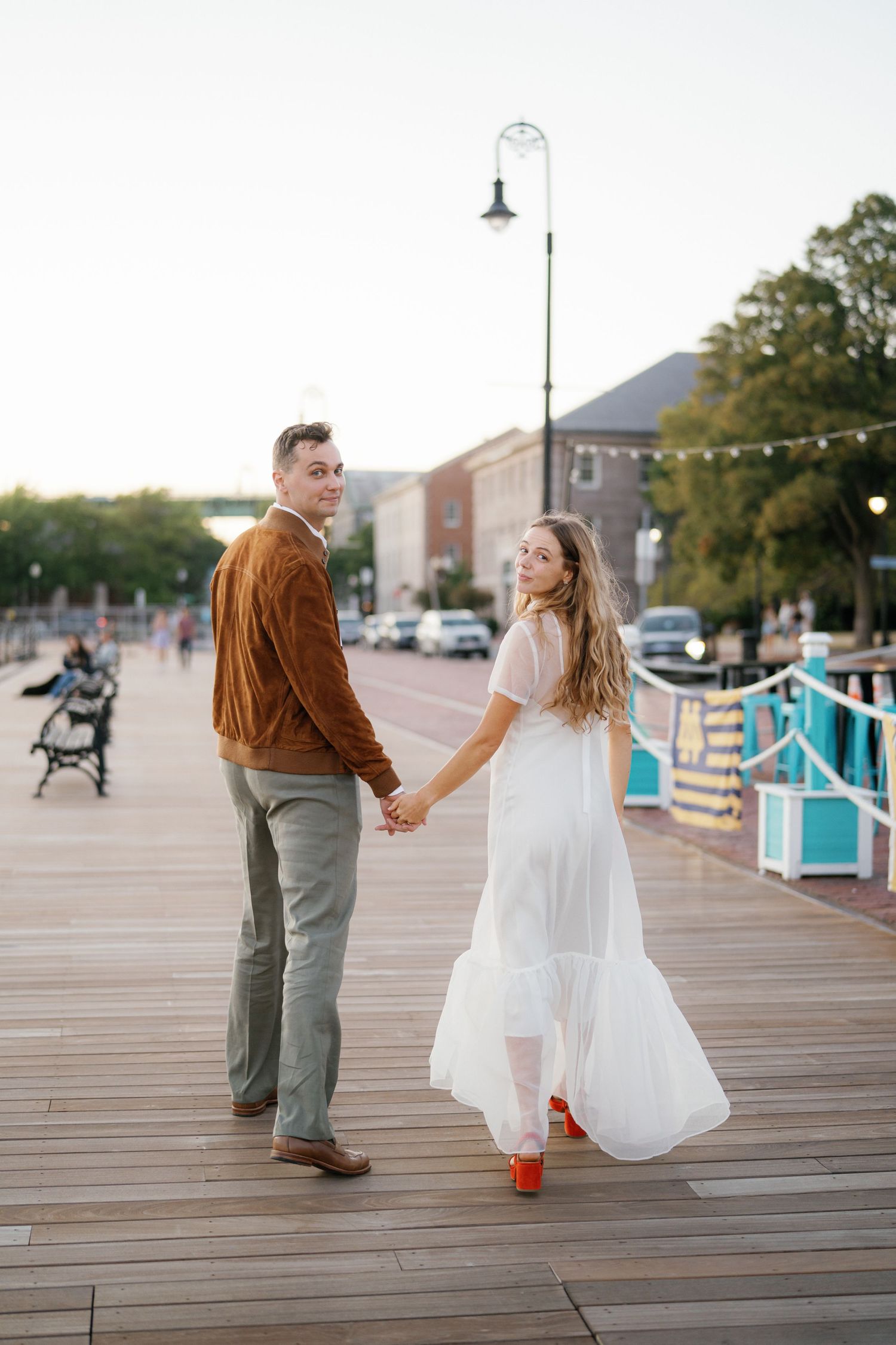 A couple dances and twirls together on a wooden boardwalk during sunset, creating a romantic seaside moment.