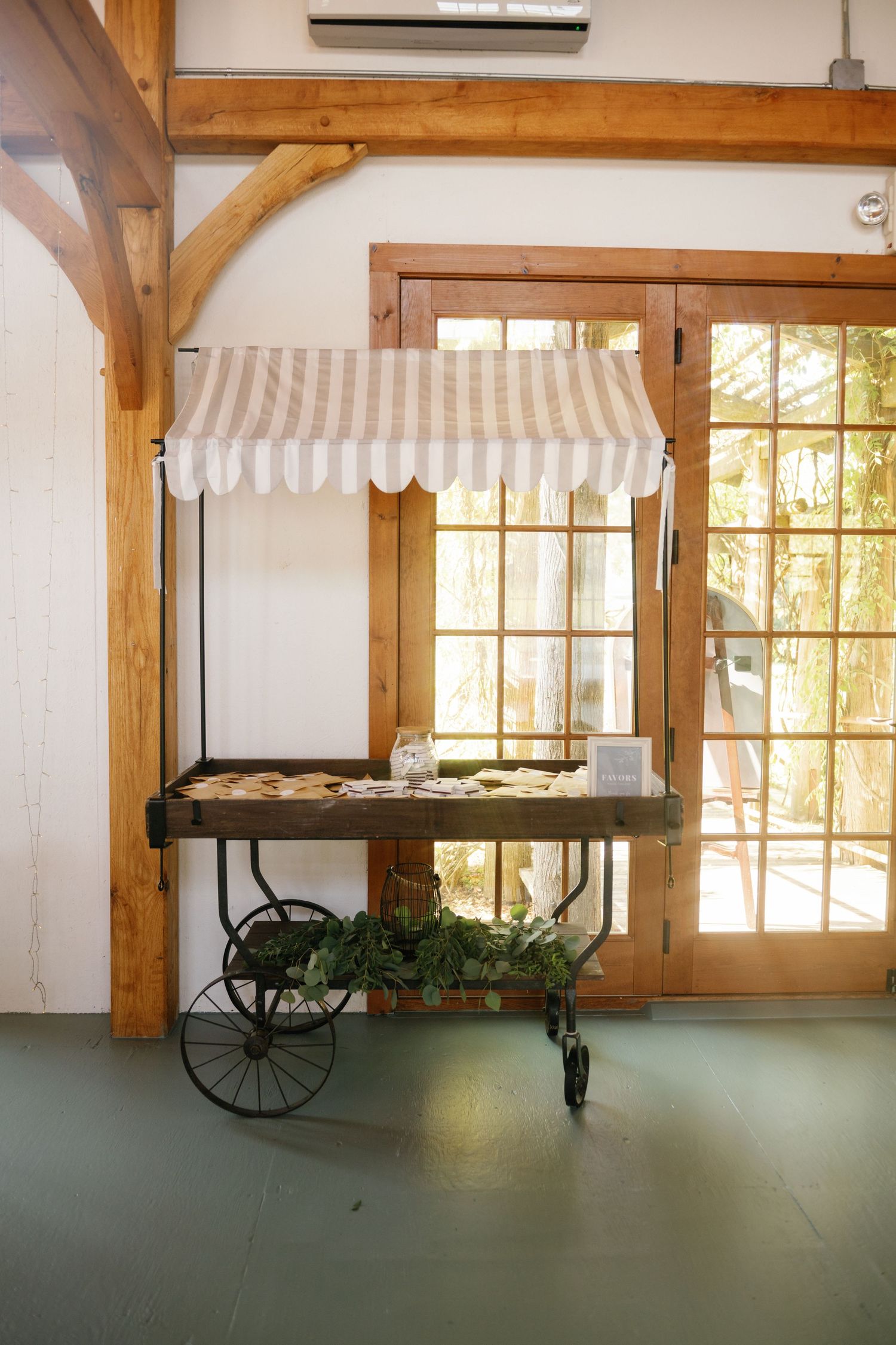 Vintage wooden cart with striped awning displayed in rustic interior space with natural lighting through windows.