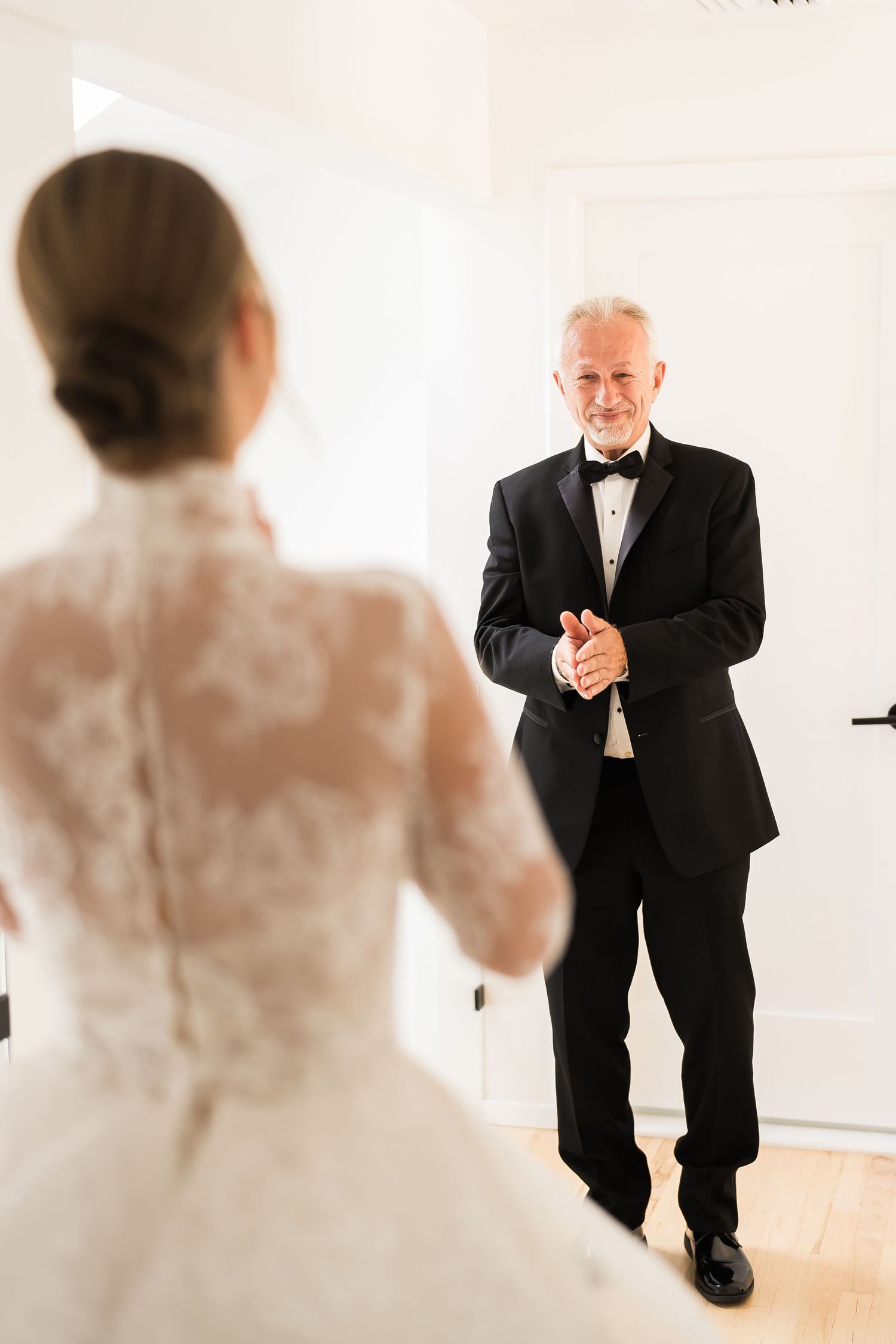 An emotional first look moment between a bride in lace and someone in a classic black tuxedo.
