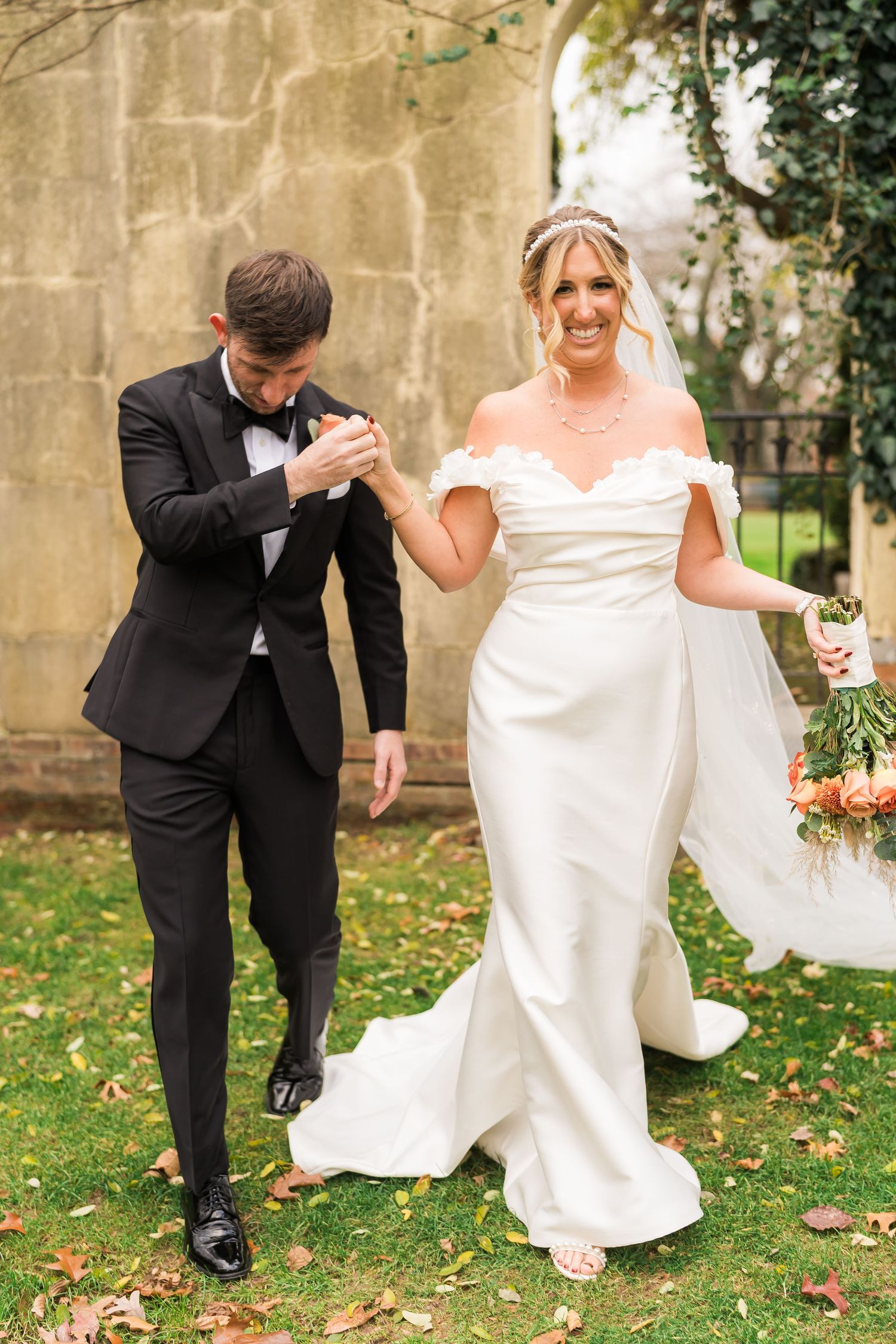 Happy couple dances on autumn grounds outside historic stone building.