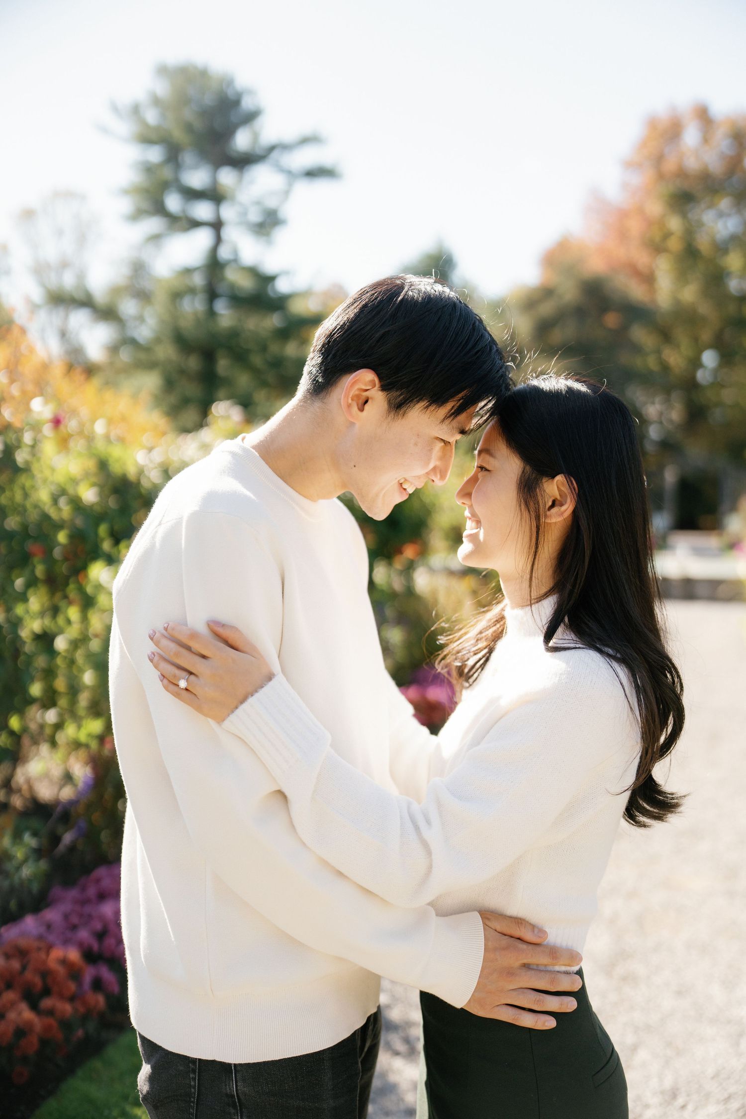 A romantic couple in white clothing embrace and dance together in a sunny outdoor garden setting.
