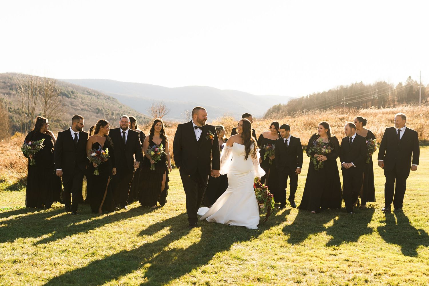 Wedding party silhouetted against scenic mountain backdrop during sunset celebration.