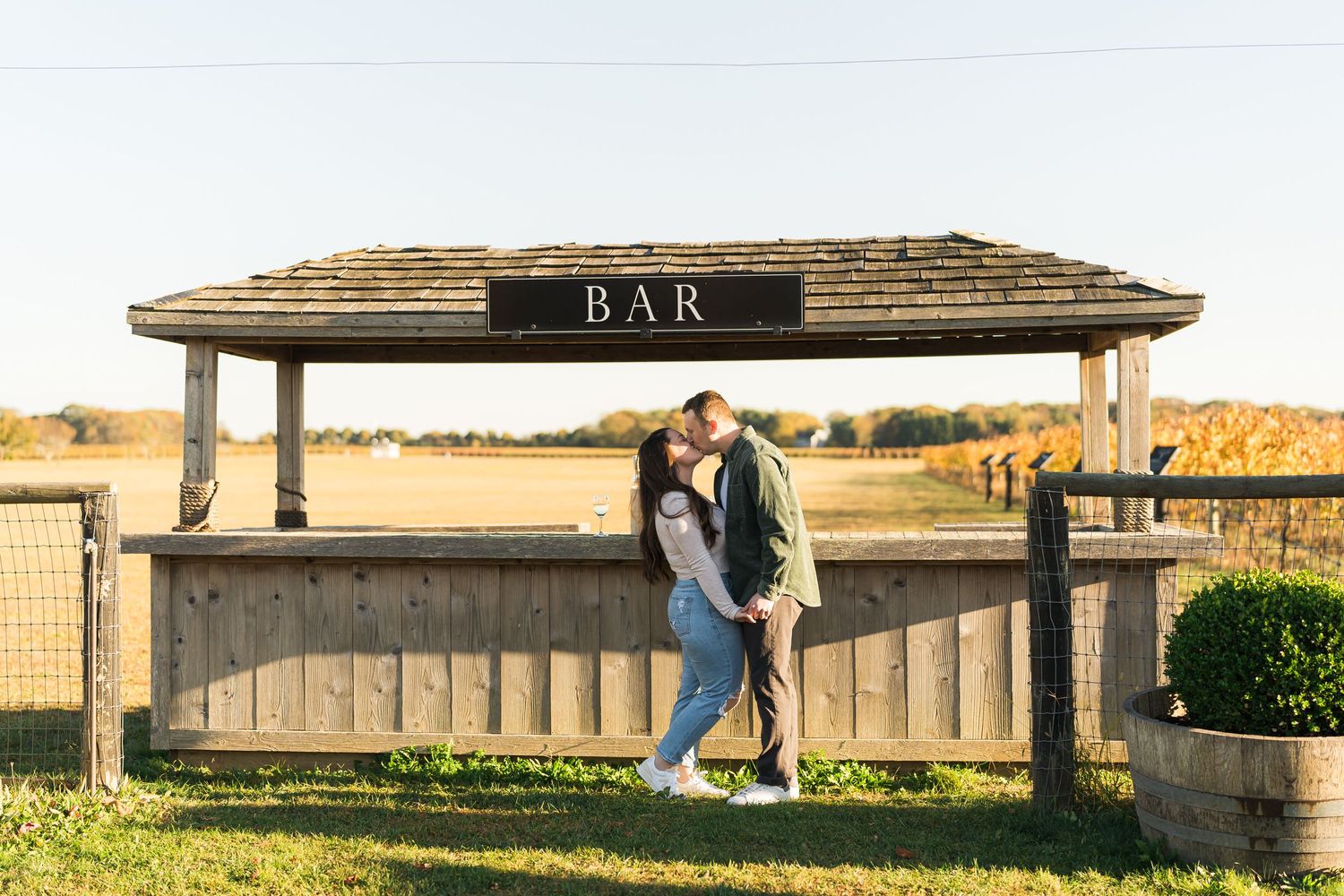 A couple embraces near a rustic outdoor bar at sunset with golden light illuminating the autumn landscape.