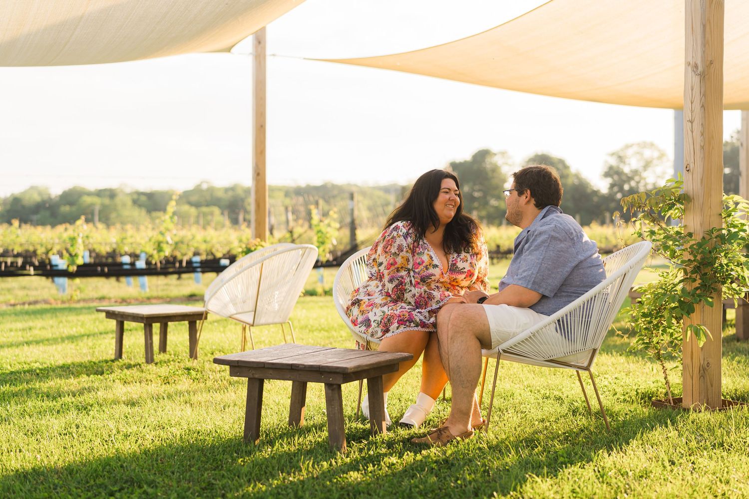 A couple enjoying wine and conversation at an outdoor vineyard lounge at golden hour.