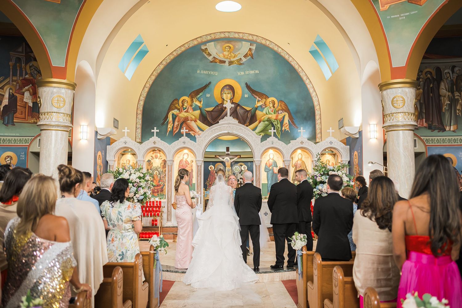Orthodox church wedding ceremony with ornate painted ceiling murals and golden religious iconography.