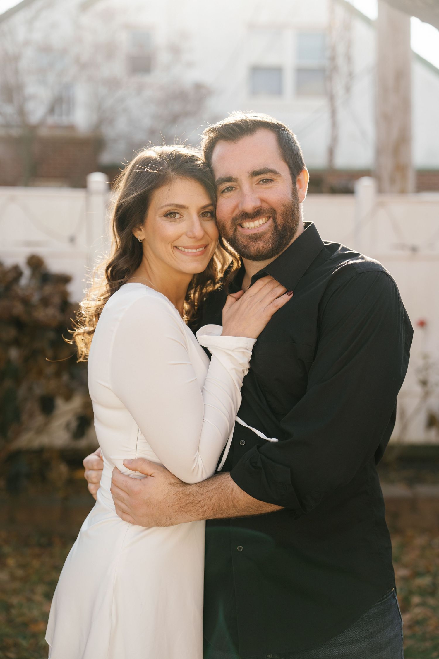 A couple in contrasting black and white outfits embrace outdoors in warm sunlight during a romantic photoshoot.