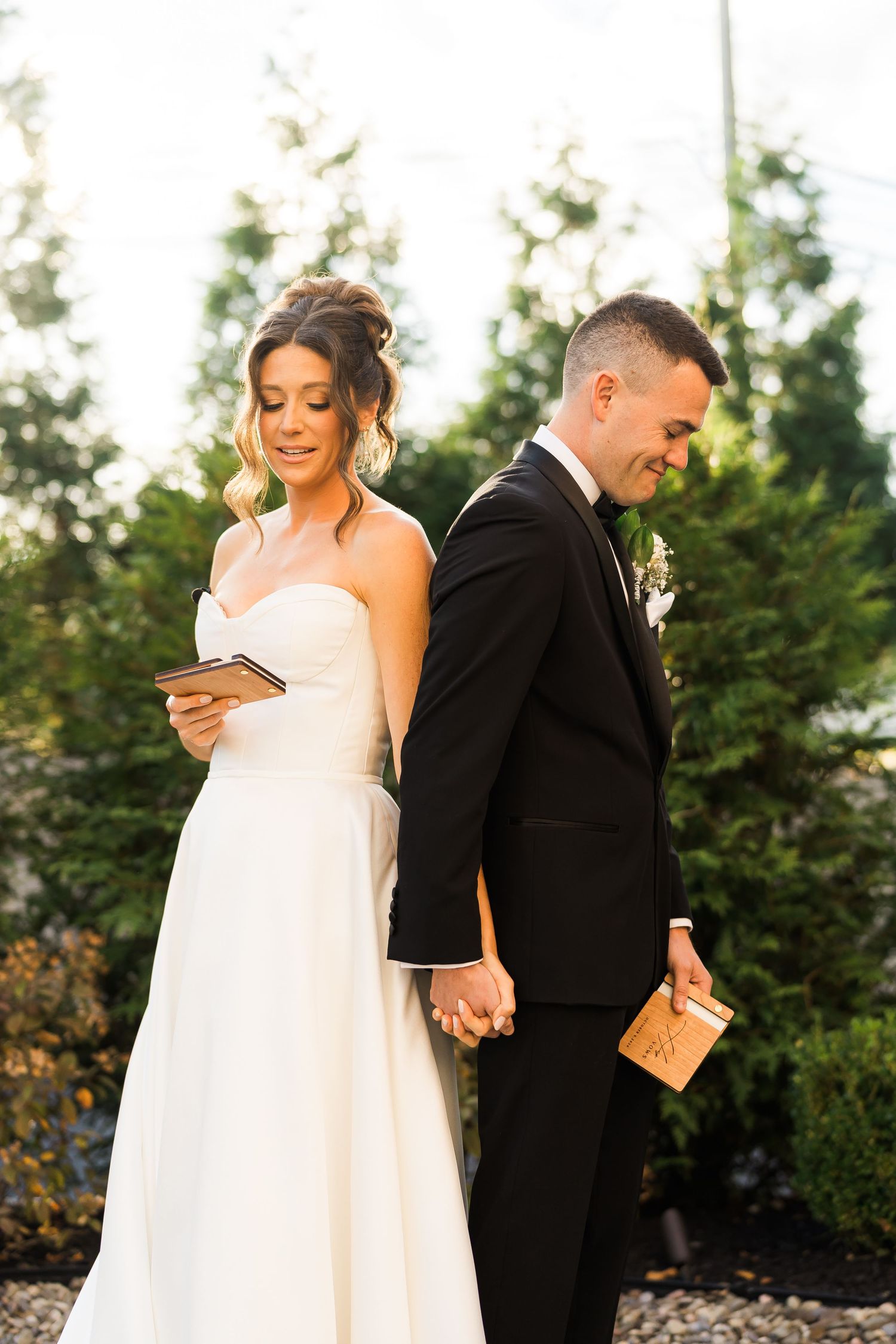 Couple stands back to back reading letters on their wedding day while holding hands.
