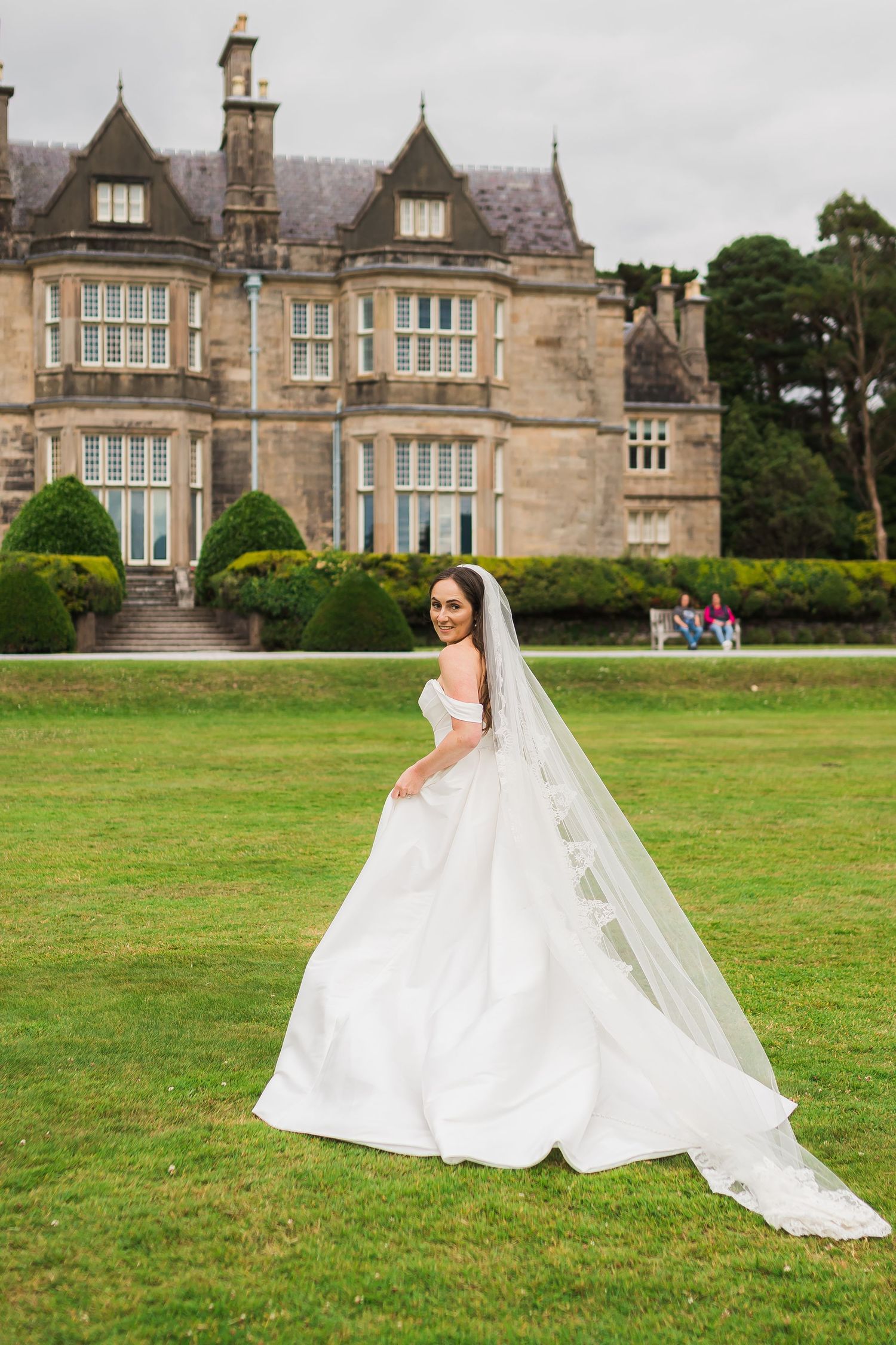 A beautiful white wedding dress with a flowing veil stands out against the backdrop of a grand historic manor house.