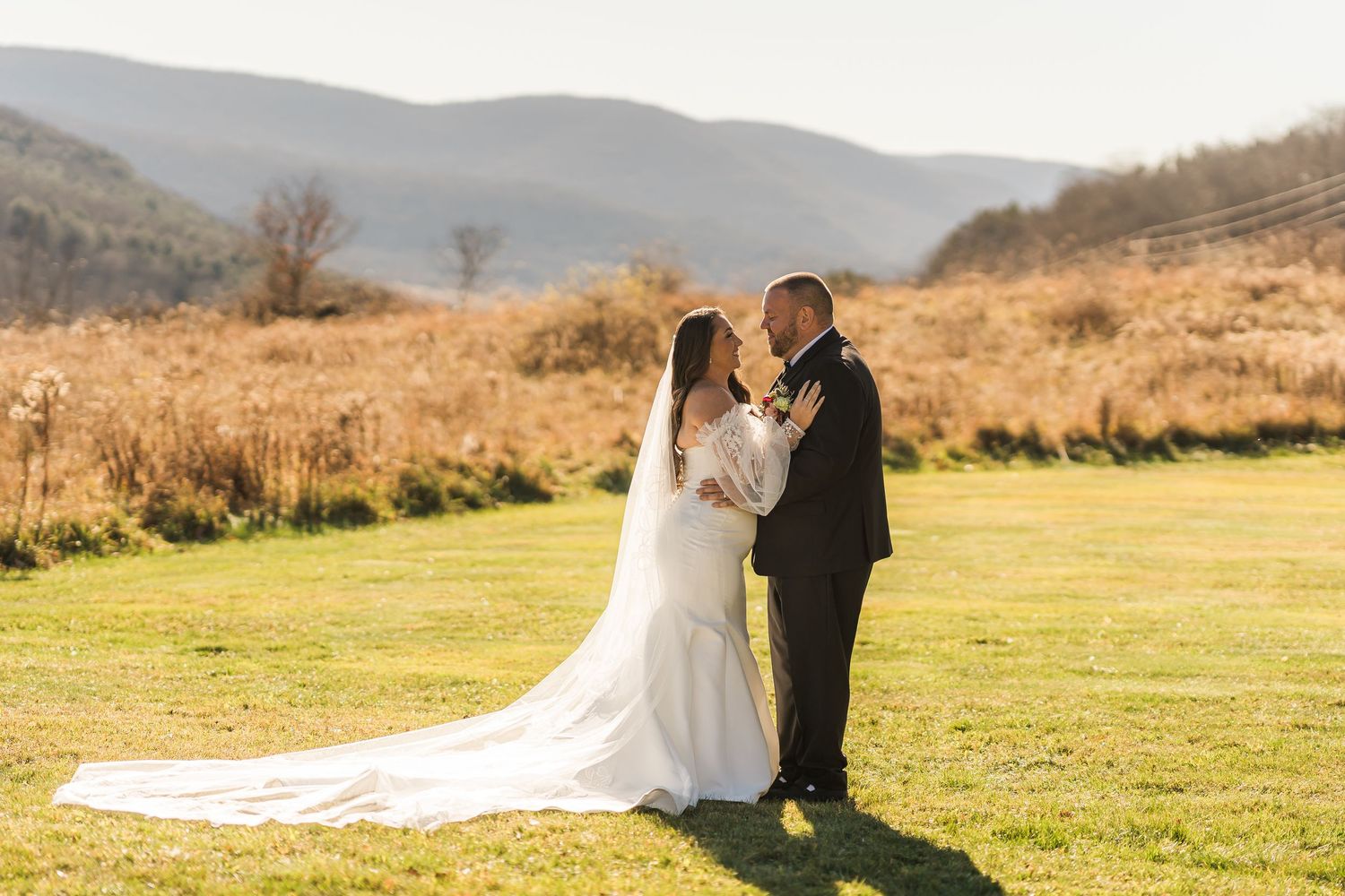 Couple shares intimate moment during sunset in field with mountains in background.