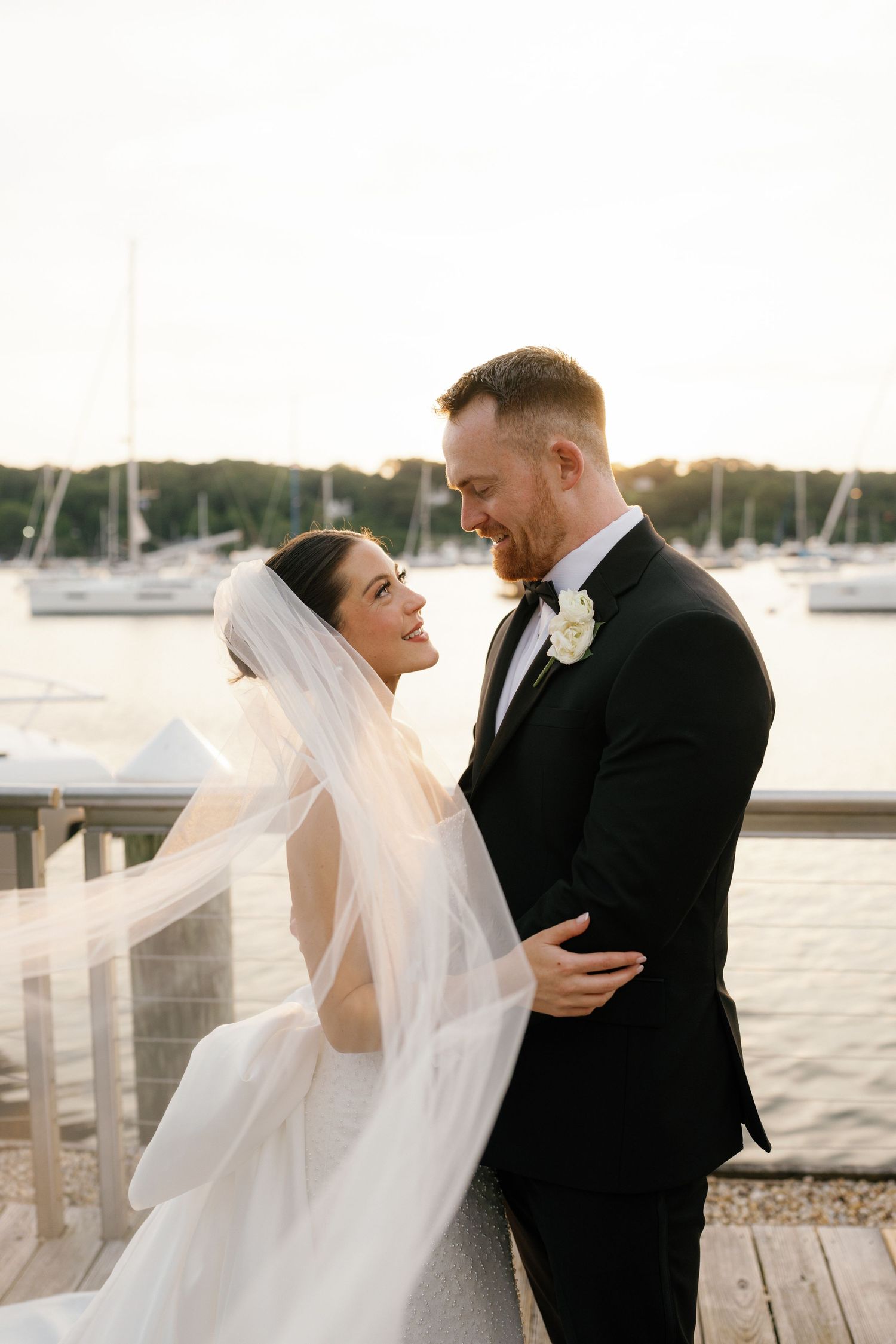 A romantic wedding couple shares intimate moments by the waterfront as a gentle breeze catches the bride's flowing veil.