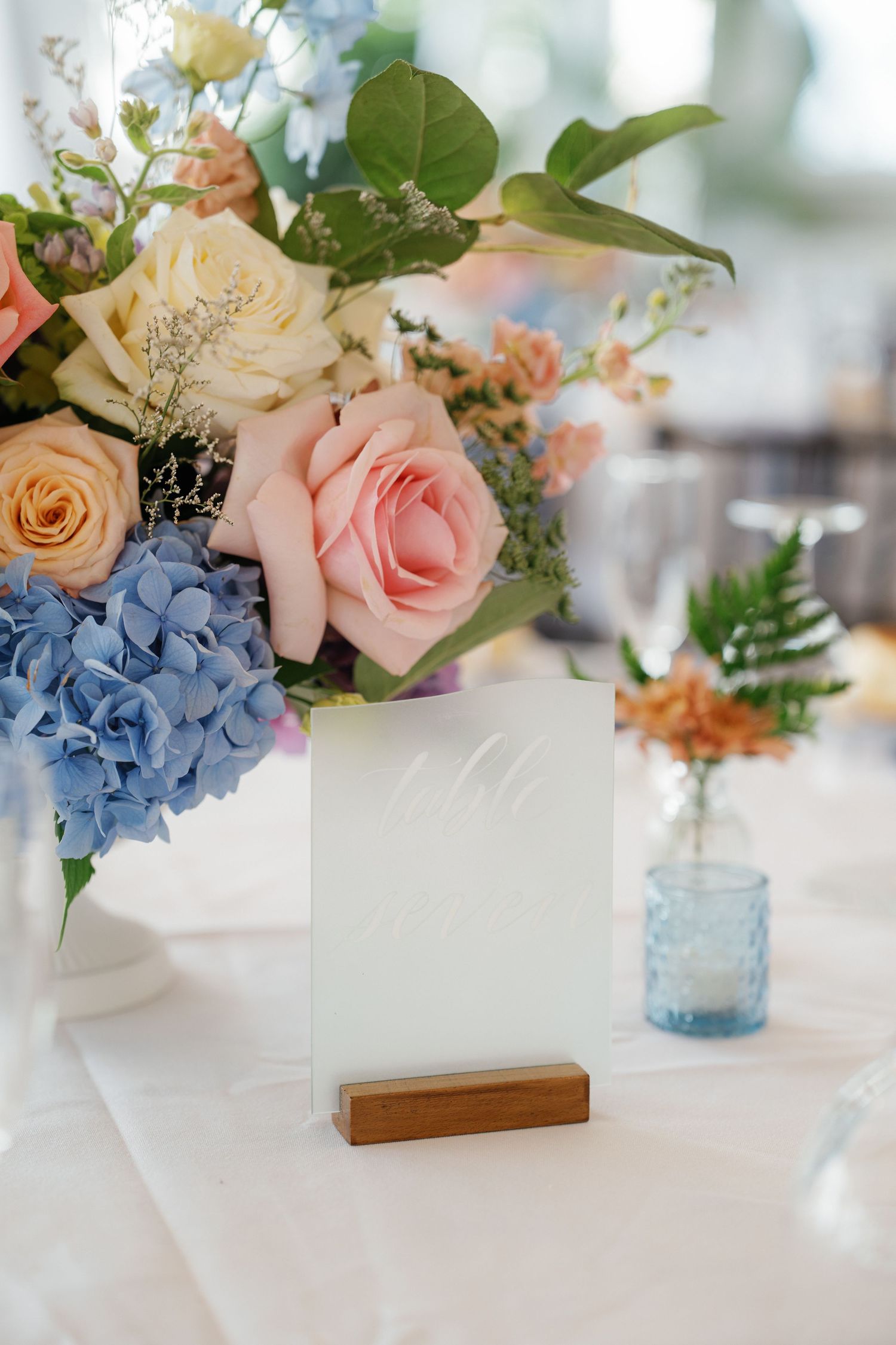 Blue hydrangeas and pink roses arranged in vintage blue mason jars as elegant wedding centerpieces on white tablecloth.