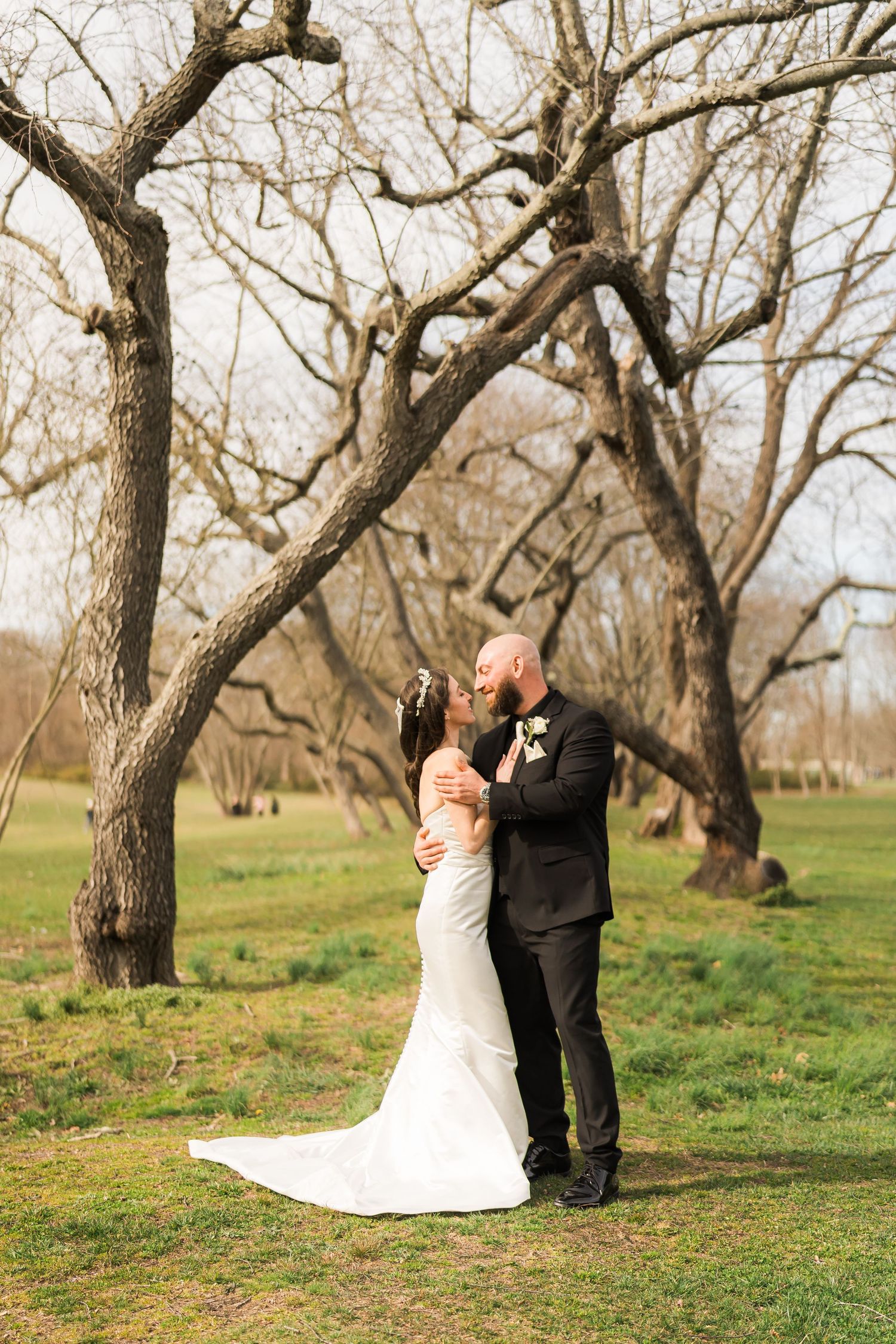 Wedding couple embraces under bare winter trees in a natural outdoor setting.