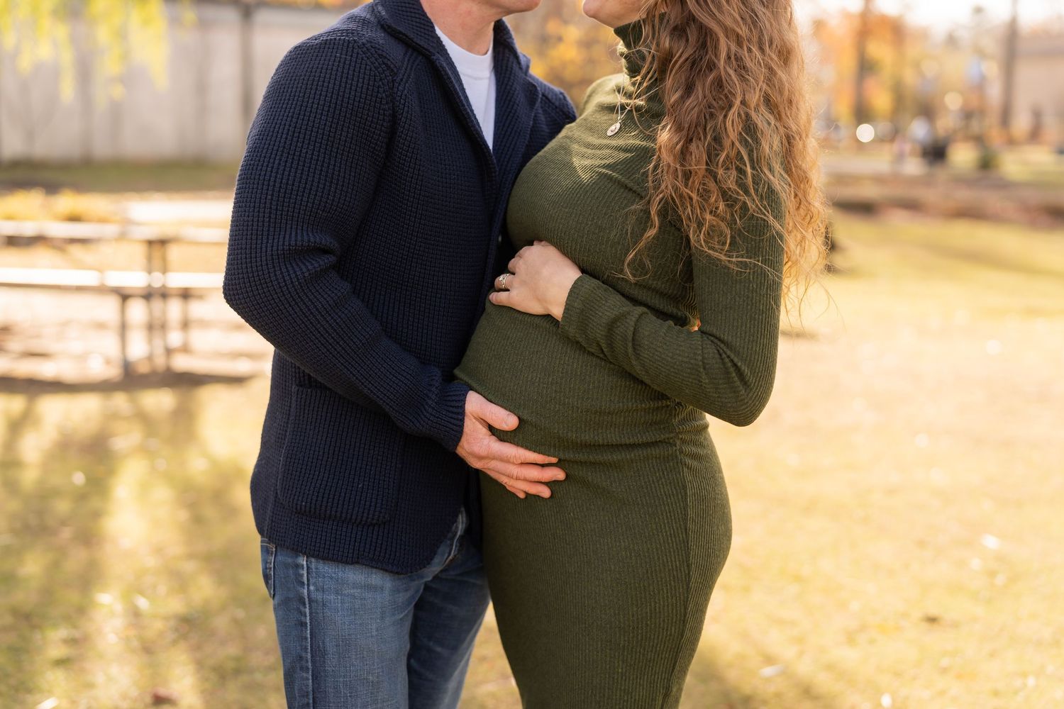 A couple embraces while expecting a baby during an autumn outdoor maternity photoshoot.
