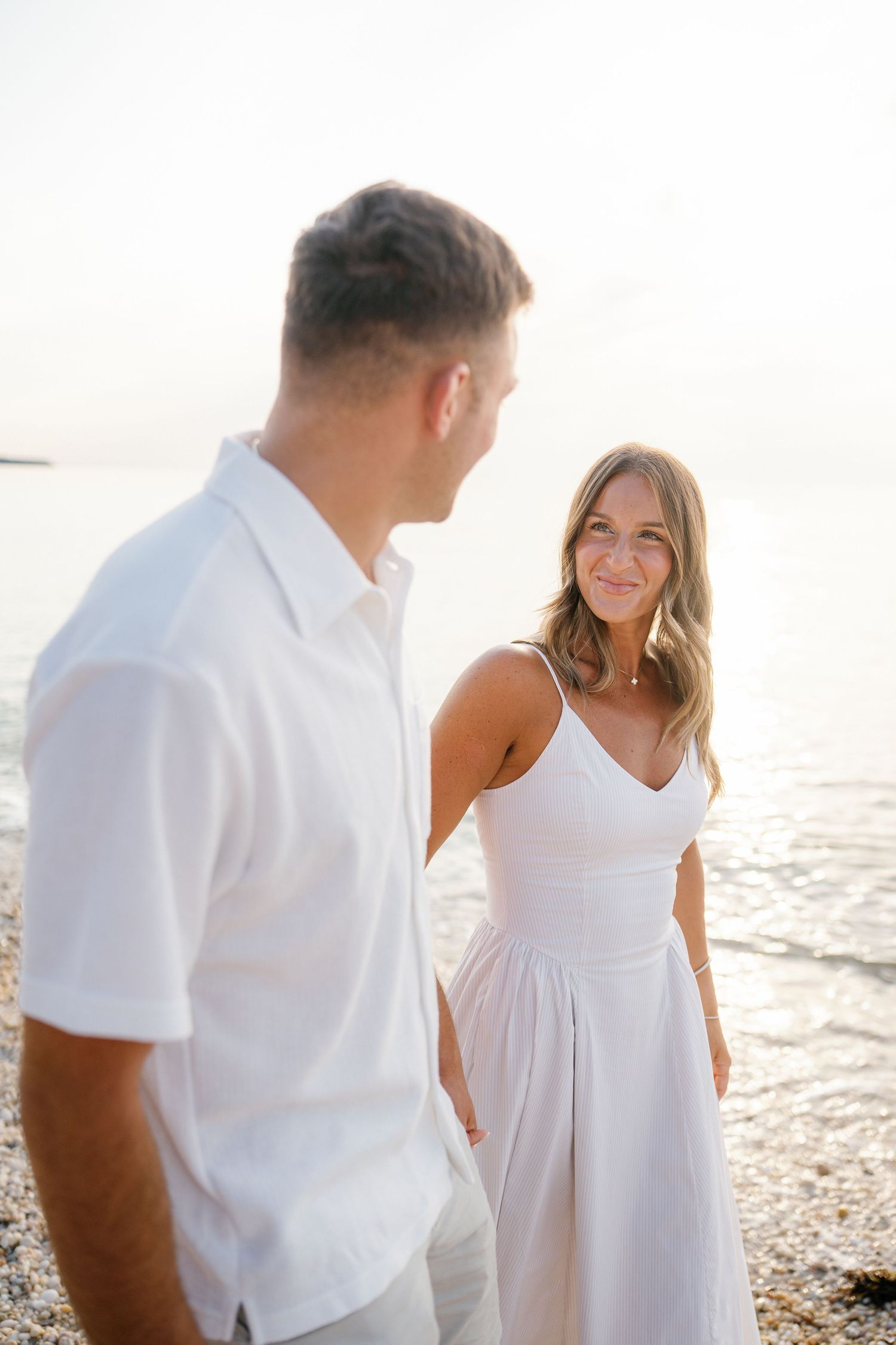 Family wearing white clothing walks together on sunny beach at sunset.