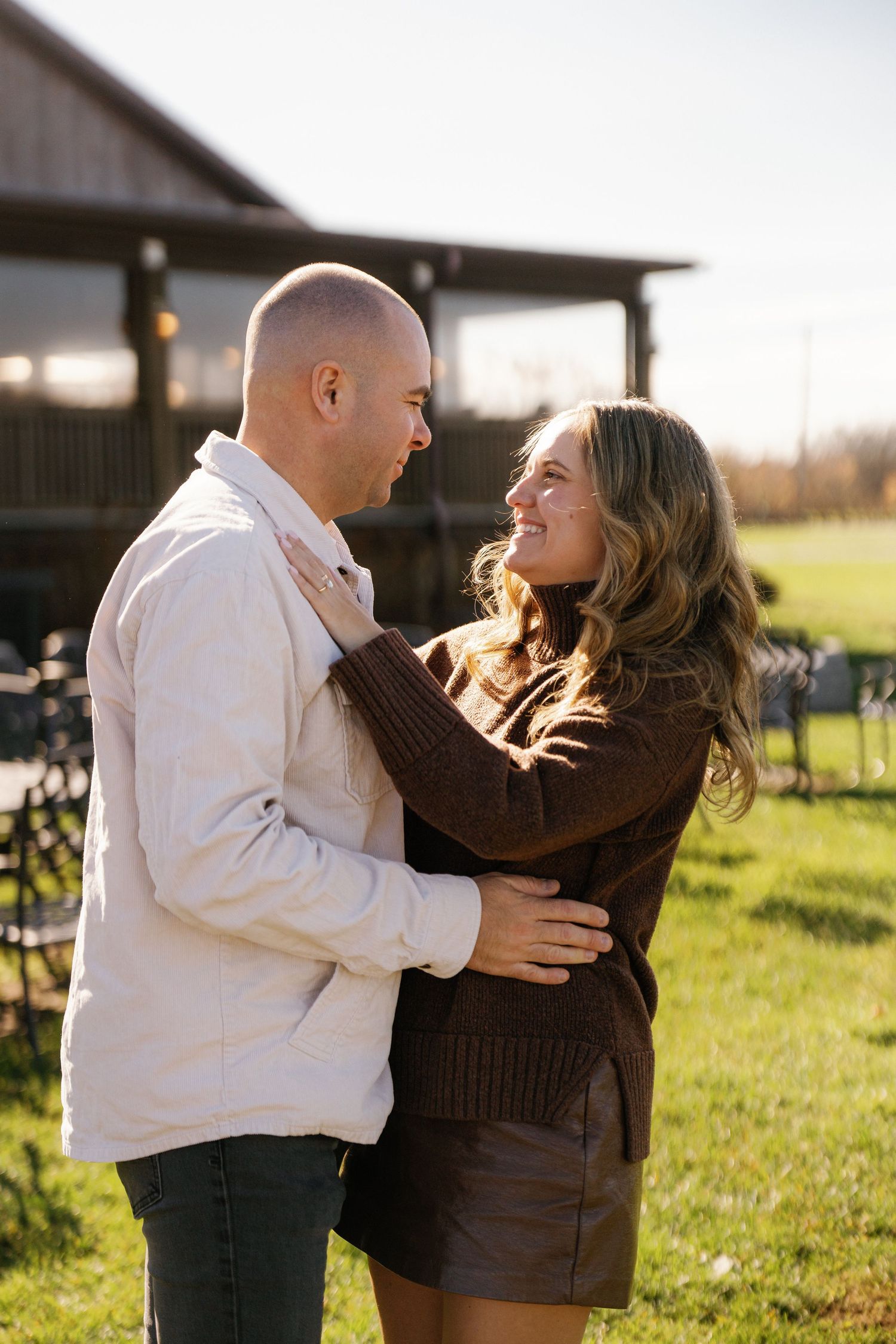 A couple laughs and plays together in a sunny field during a romantic photoshoot at golden hour.