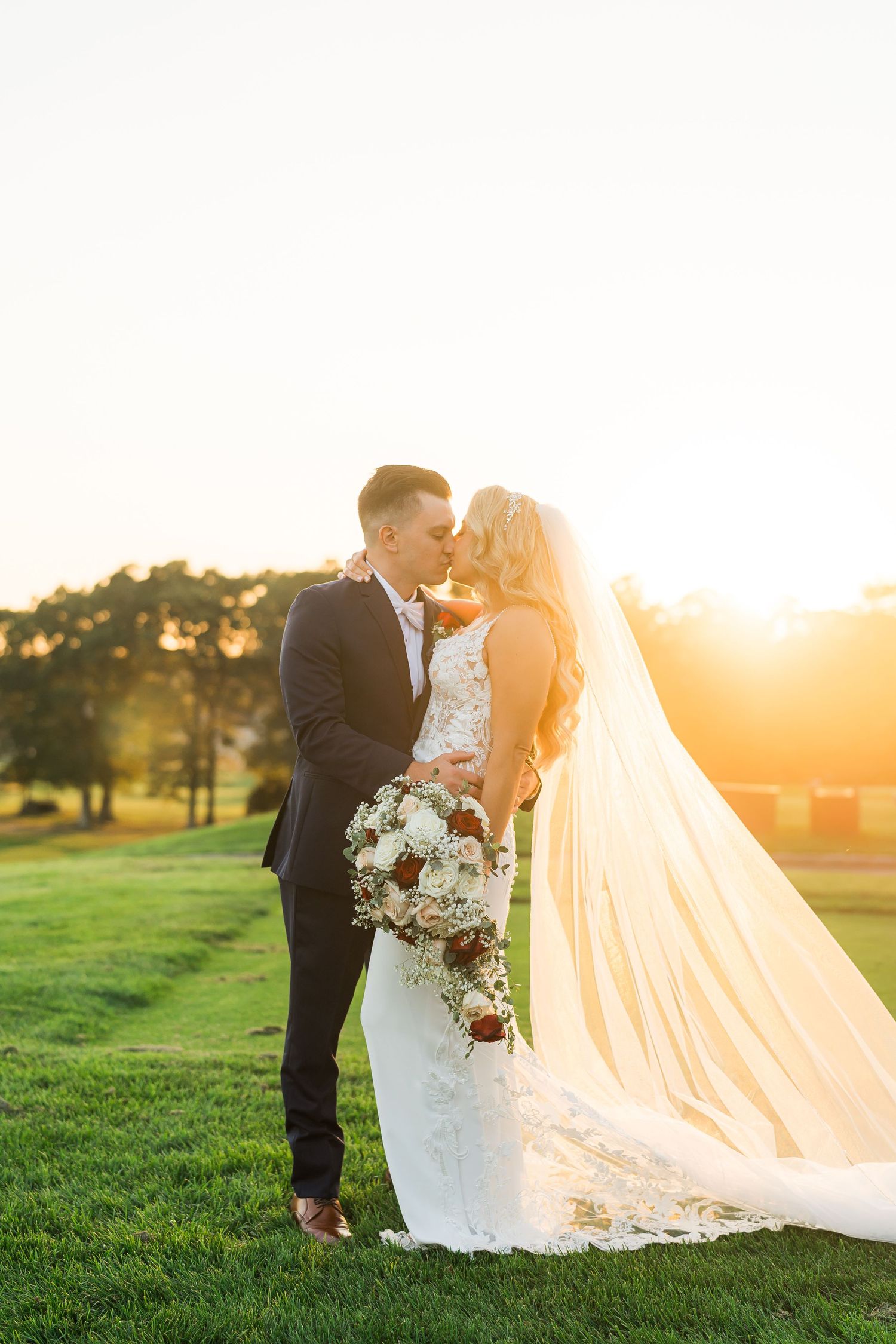 A romantic sunset wedding portrait with flowing veil and floral bouquet.