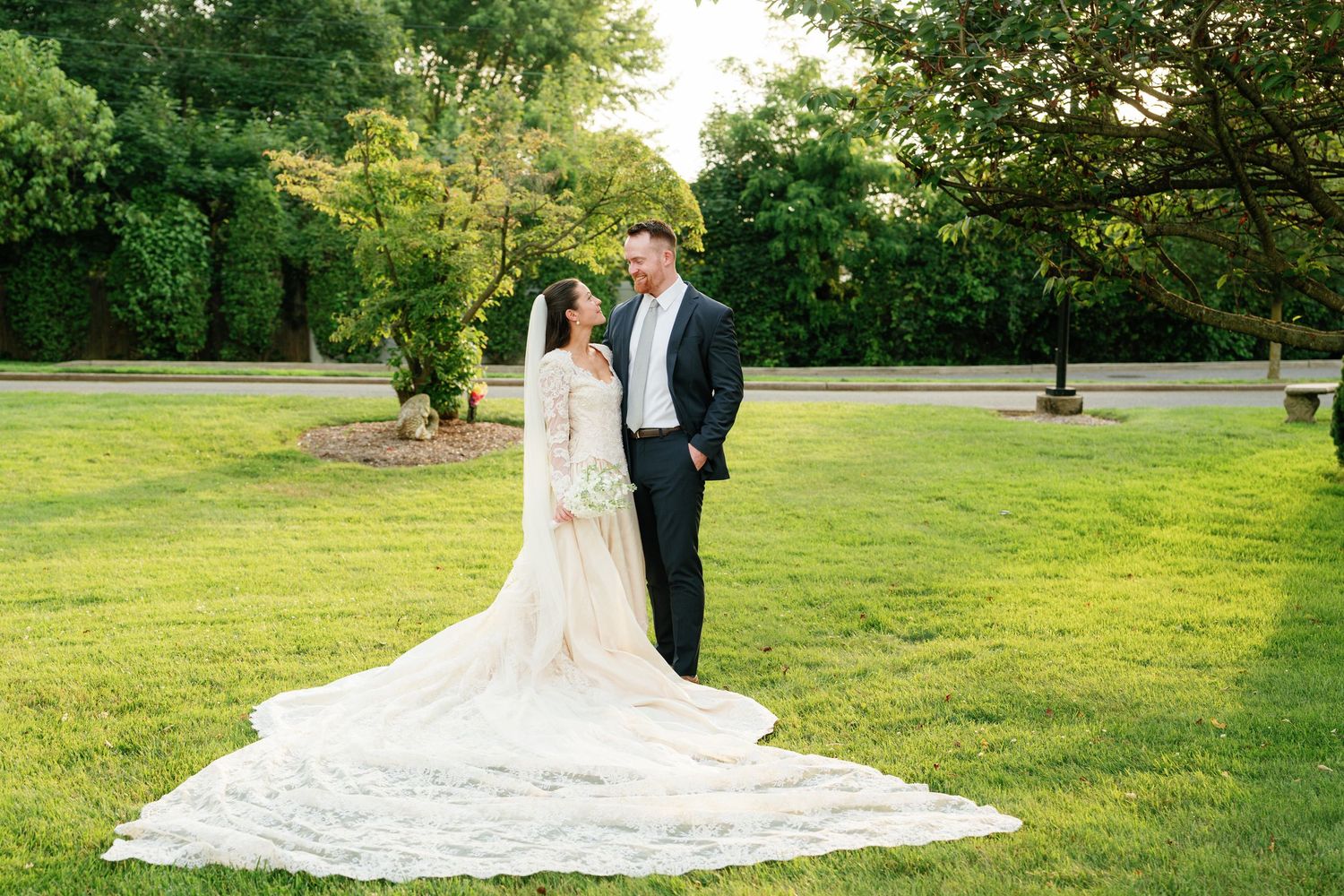 A couple in wedding attire walks together through a lush green garden setting on their special day.