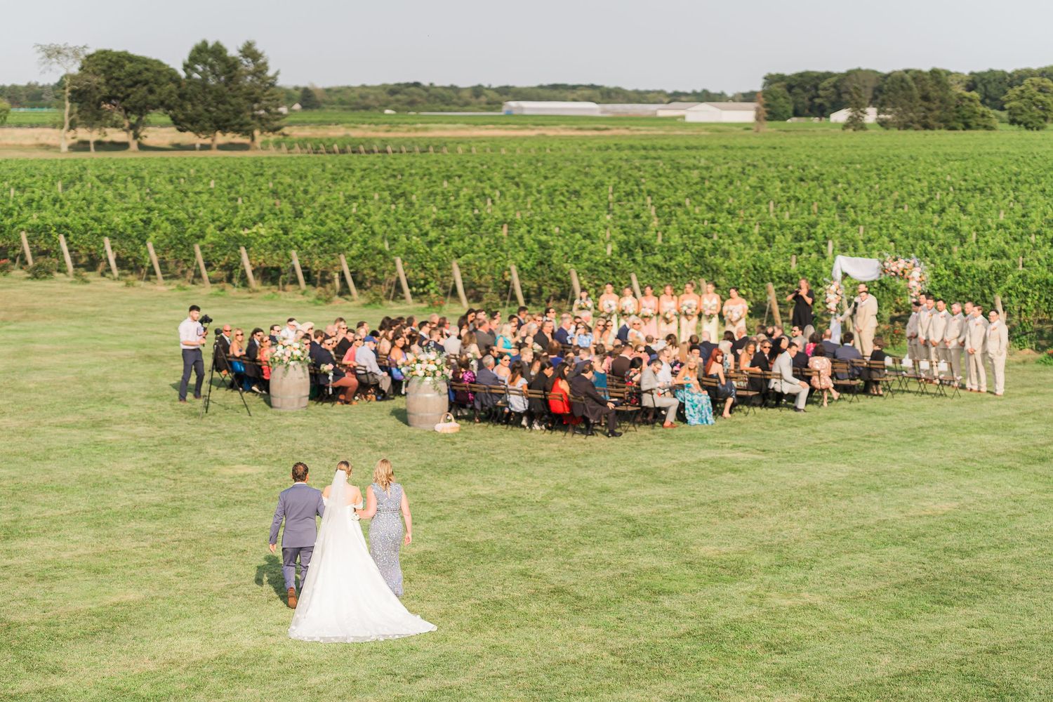 Wedding ceremony set up on a lush green lawn with vineyard views in the background and guests seated in white chairs.