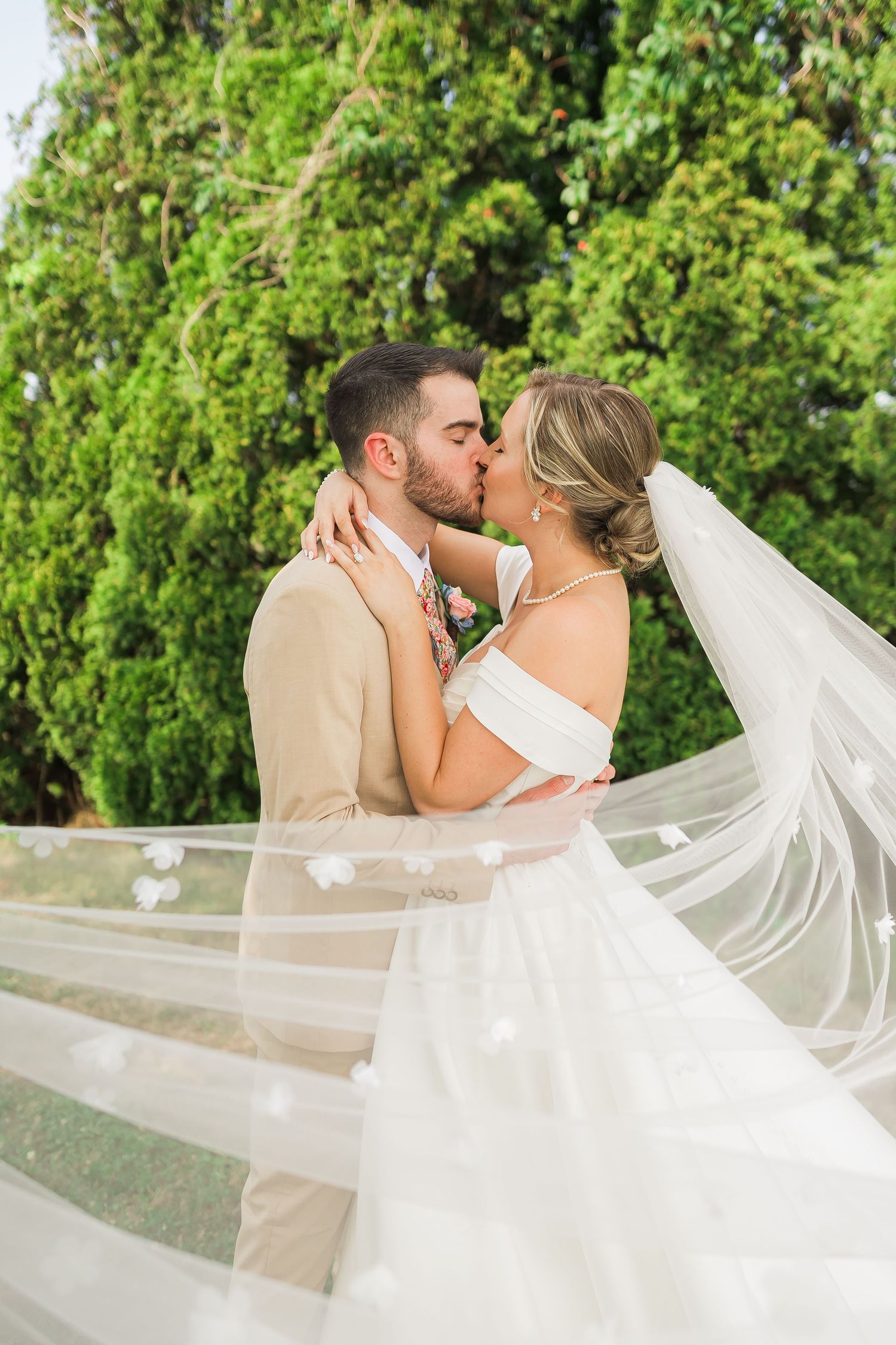 Romantic wedding portrait with flowing veil catching the breeze during couple's kiss.