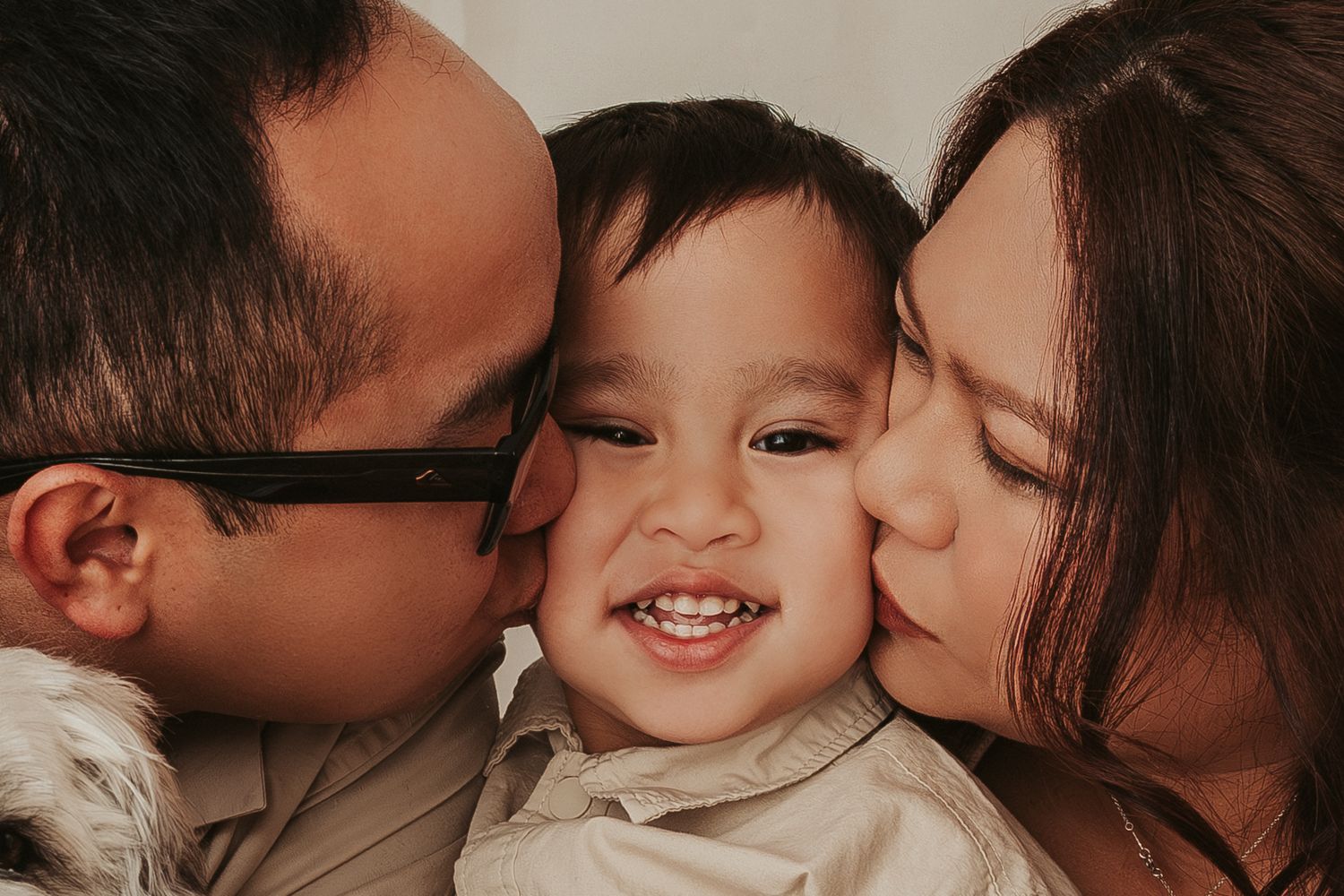 A series of five loving family photos showing parents kissing their toddler child in intimate close-up shots.