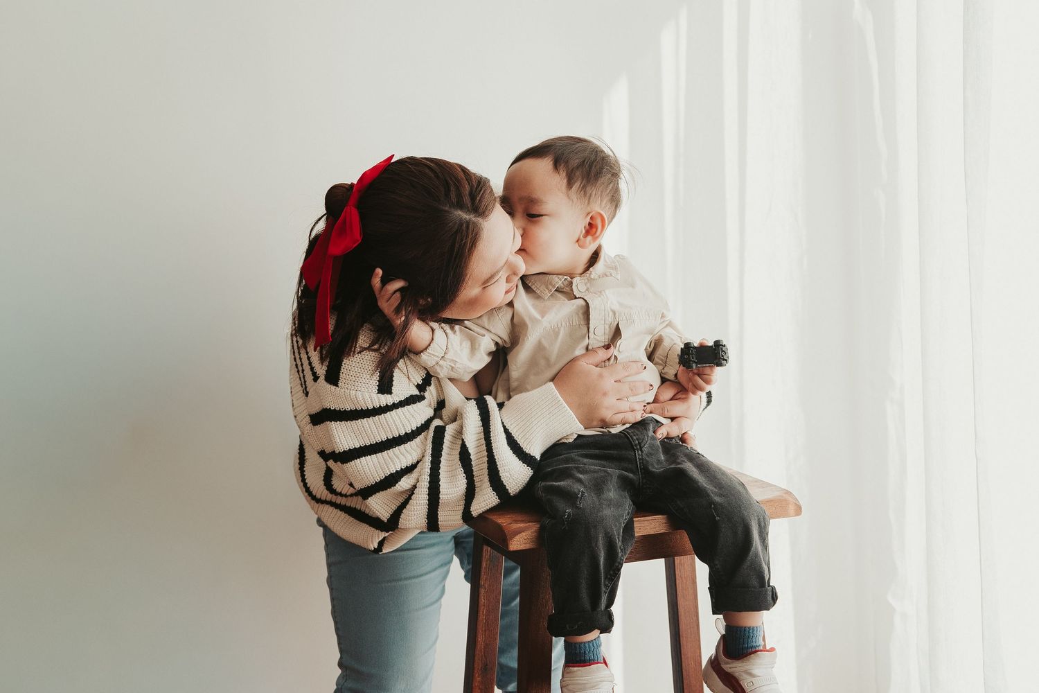 Parent and child share tender playful moments in white minimalist setting with loving interaction and bright natural light.