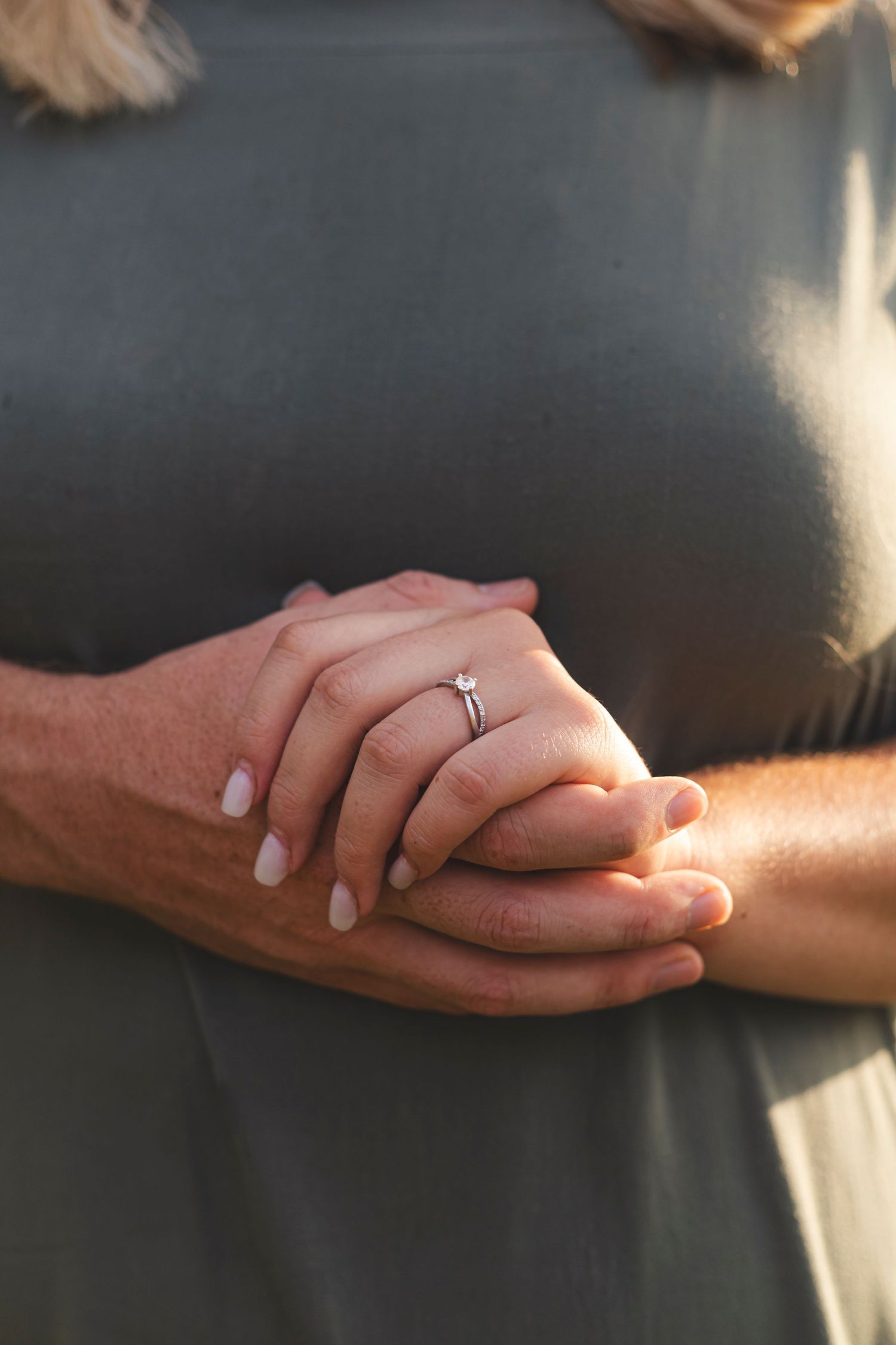 Close up of hands clasped together with engagement ring, showing tender affection and commitment.