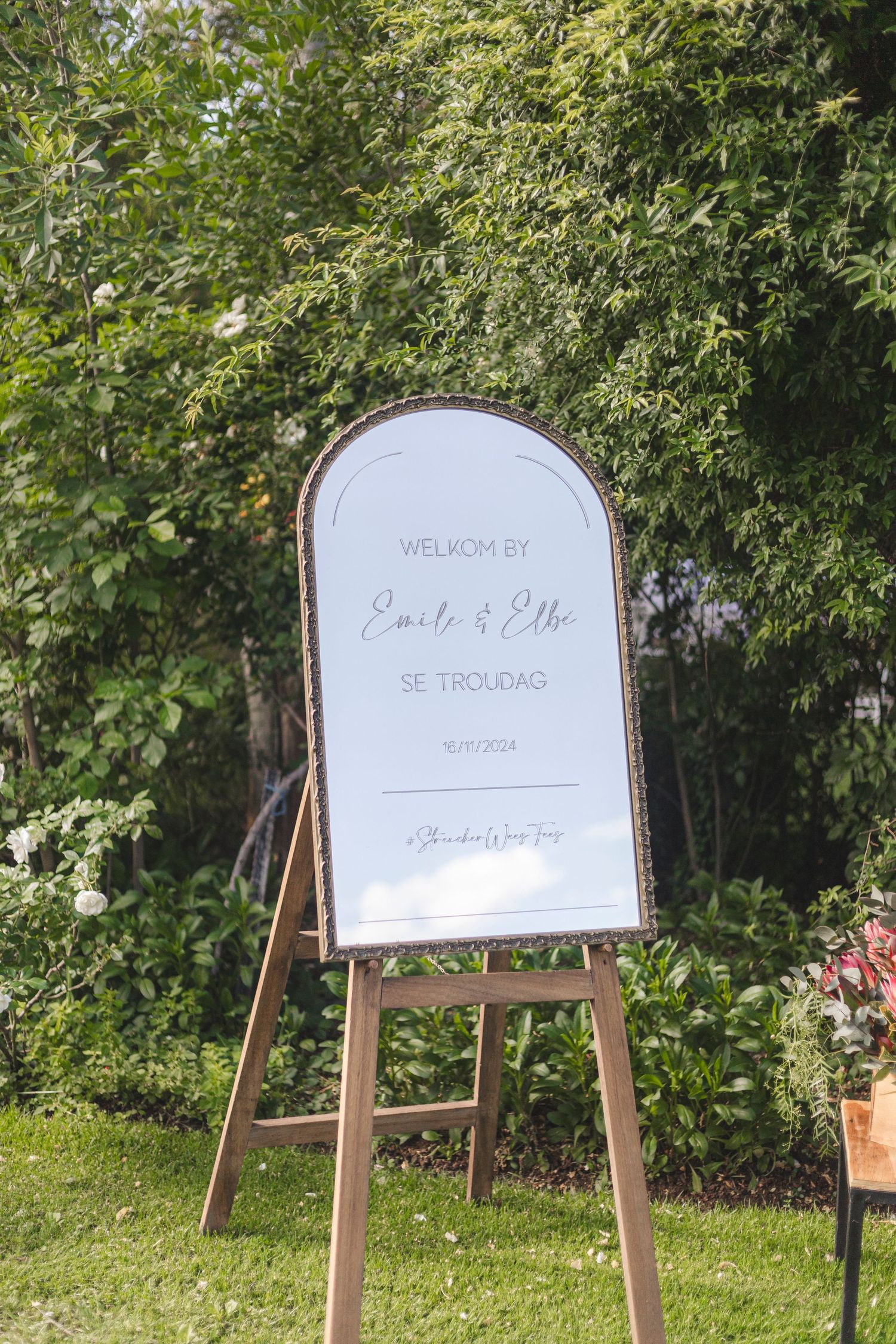 Wedding welcome sign on wooden easel displayed in lush garden setting.
