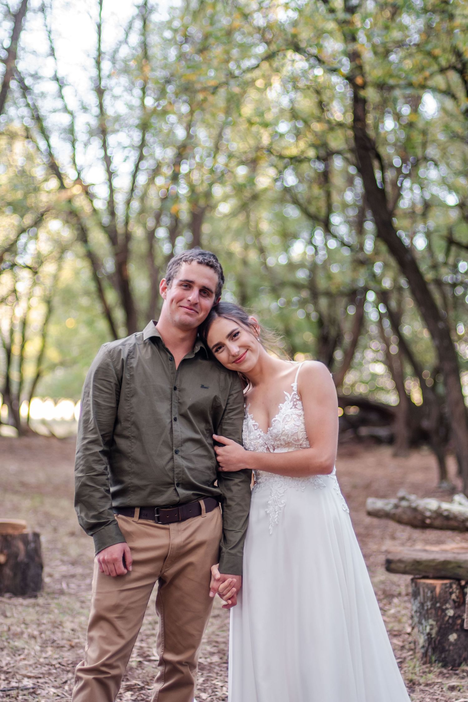 A couple poses together in a wooded forest setting during autumn.