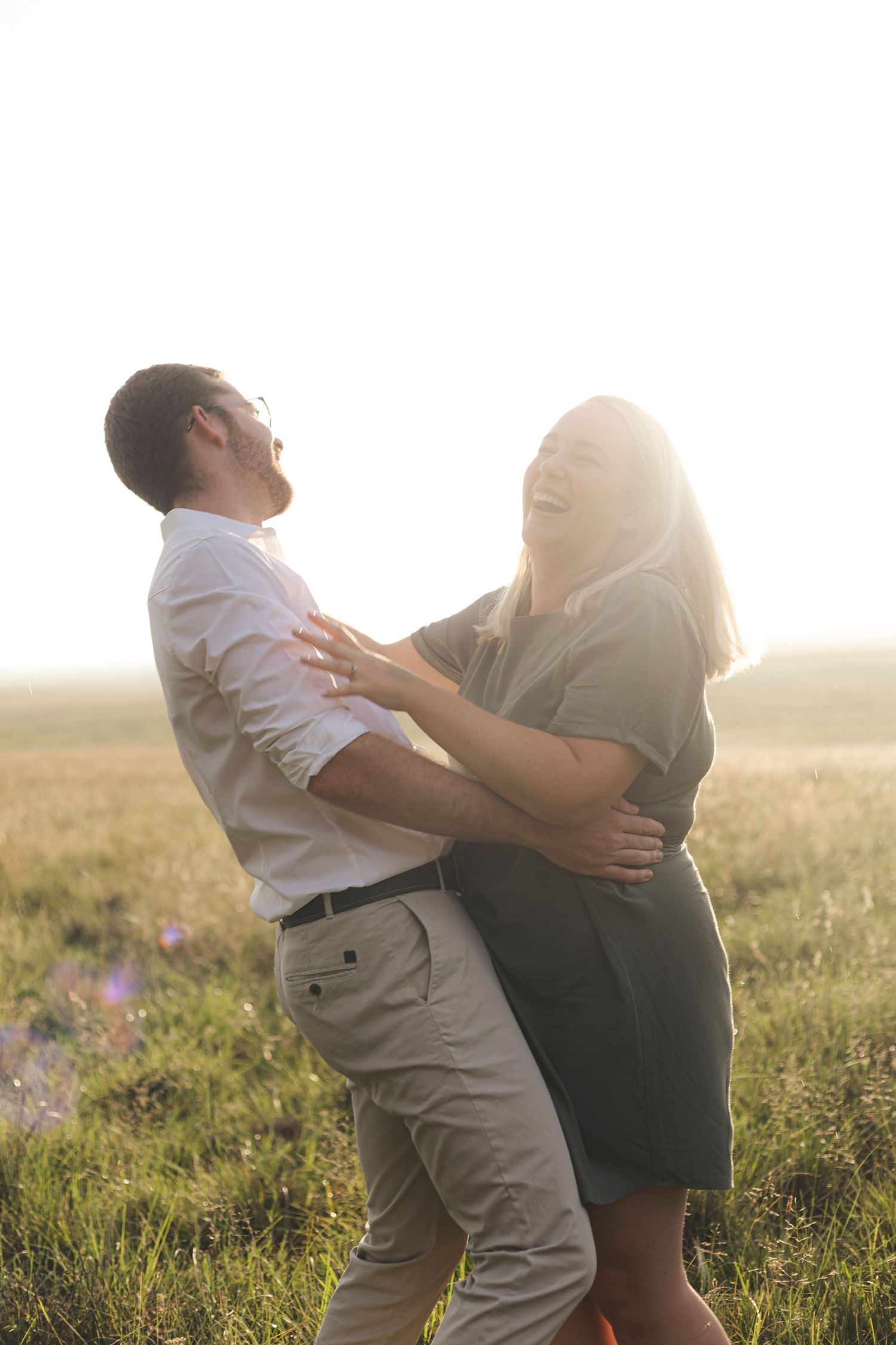 Couple embracing in a sunlit meadow during golden hour with dramatic backlit silhouettes.