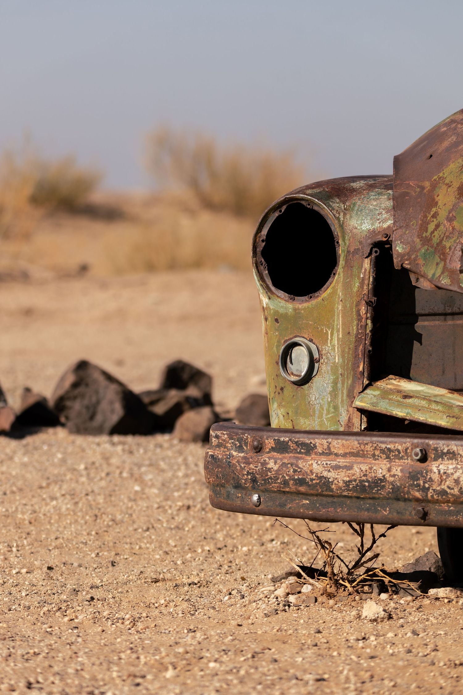 Rusty vintage car headlight in abandoned desert setting with rocky terrain.