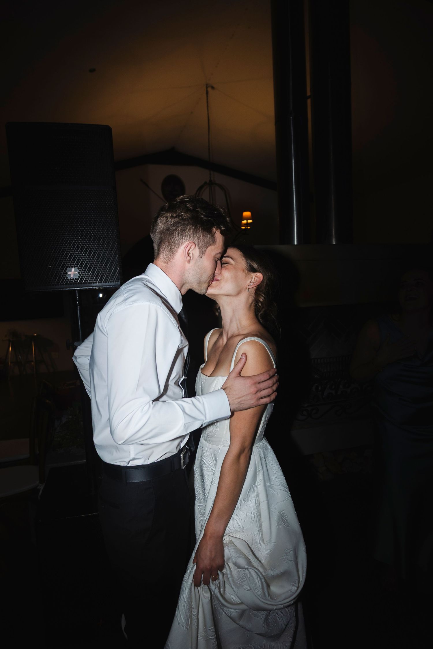 A bride and groom share a romantic first dance kiss in a dimly lit wedding reception venue.