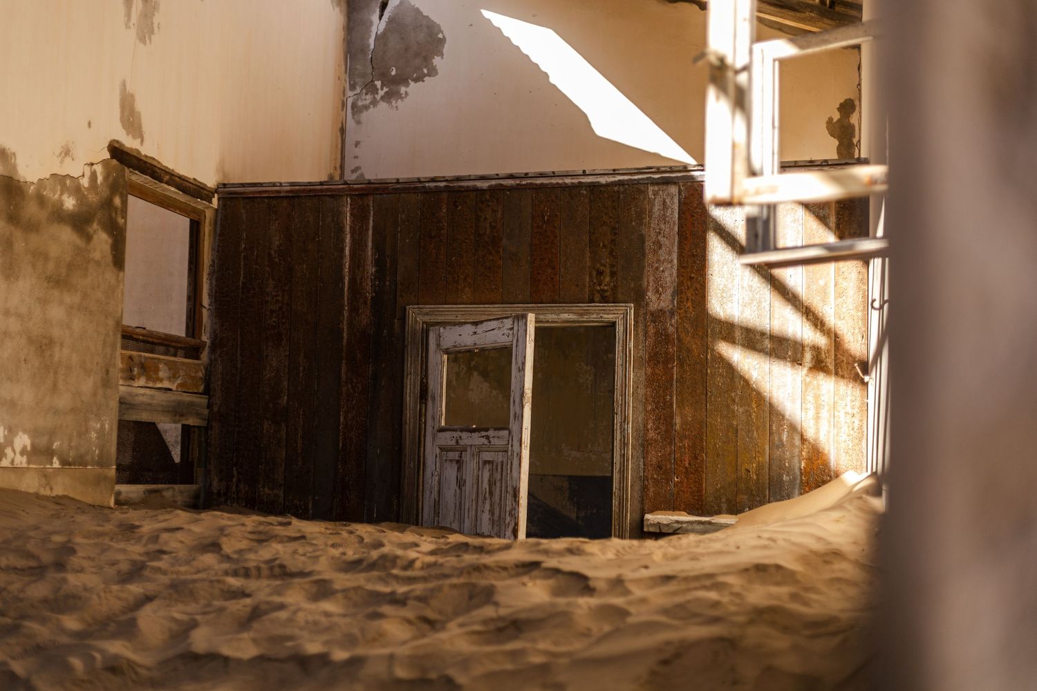 Sand-filled doorway of abandoned building with sunlight casting dramatic shadows.