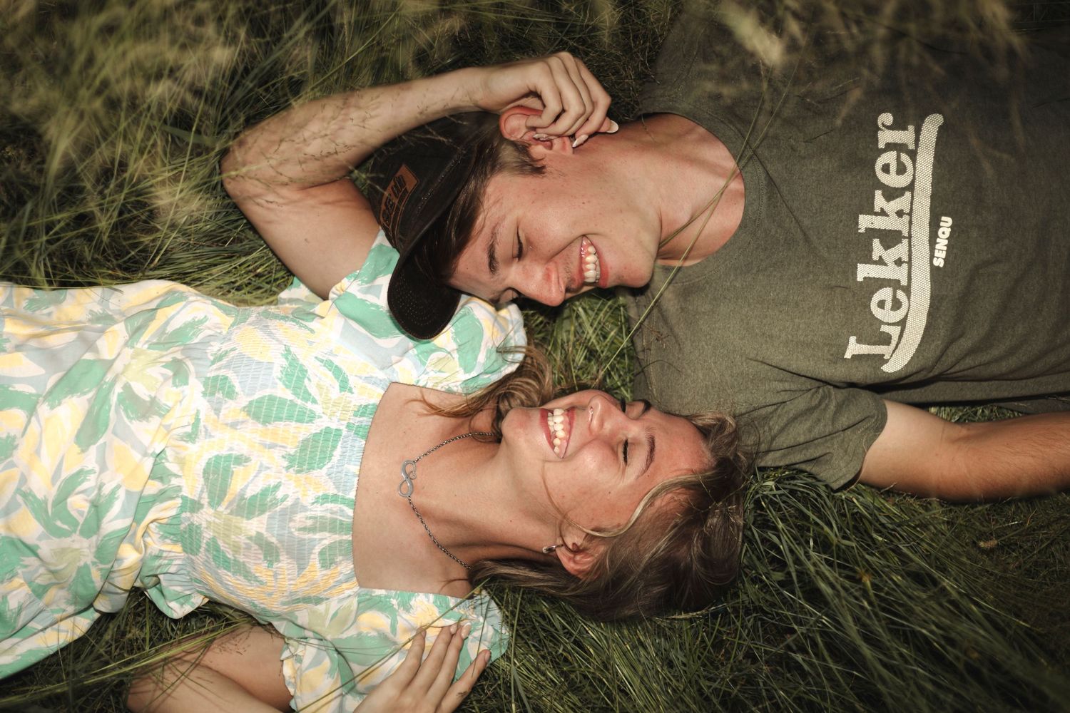 Couple laying in grass laughing together in romantic outdoor photoshoot.