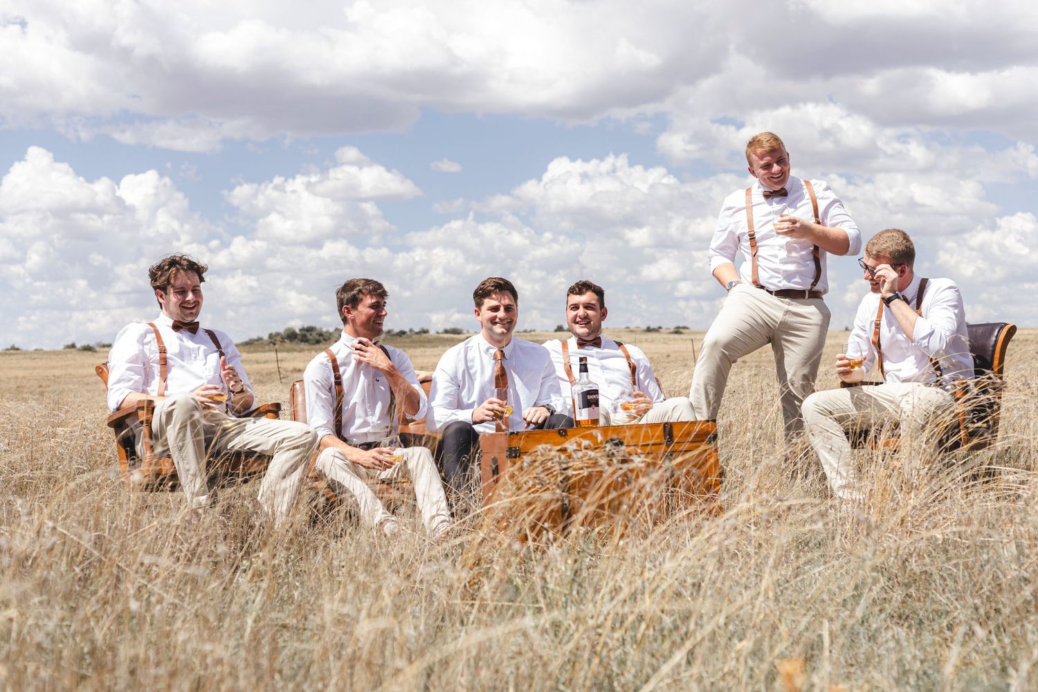A group sits together in a golden wheat field on a sunny day with white clouds in the background.